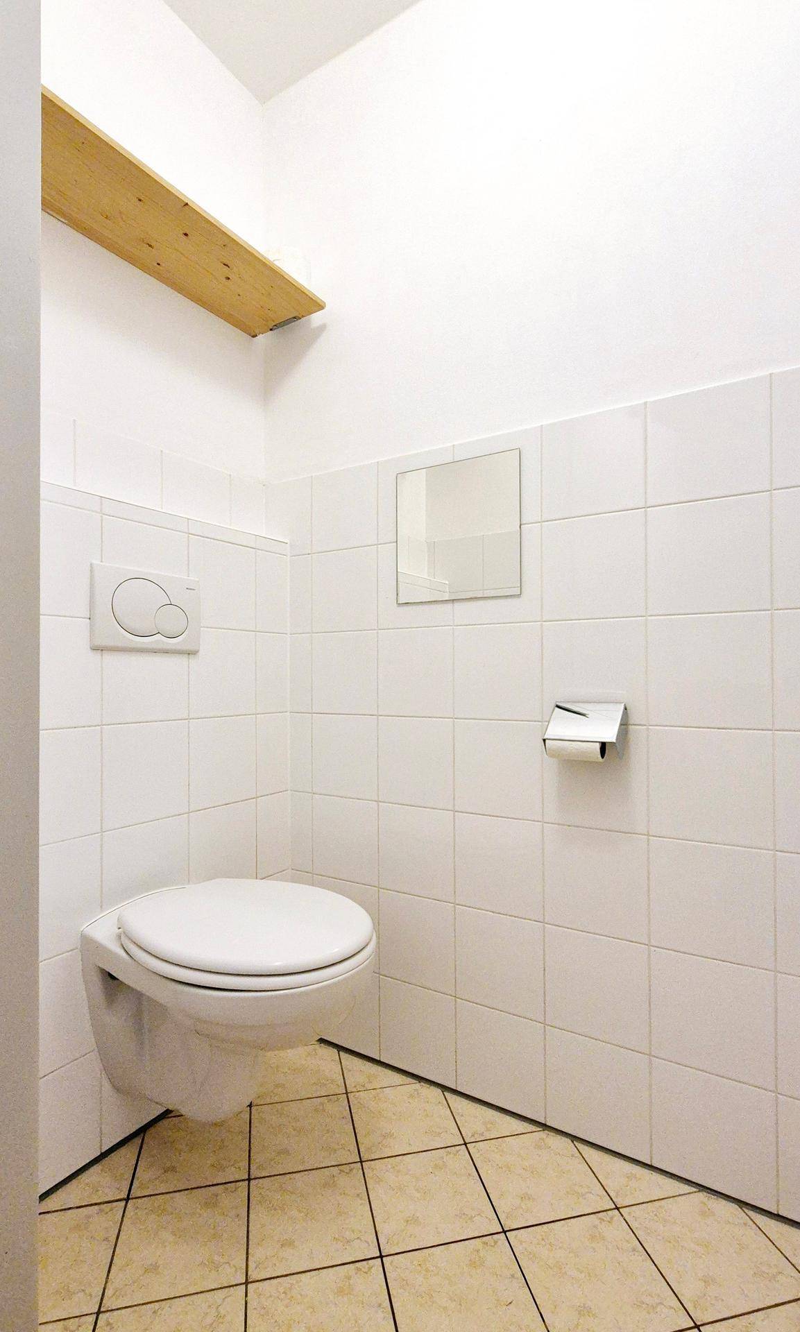 Kleines WC mit wandhängender Toilette und weißen Fliesen an Wänden und Boden.