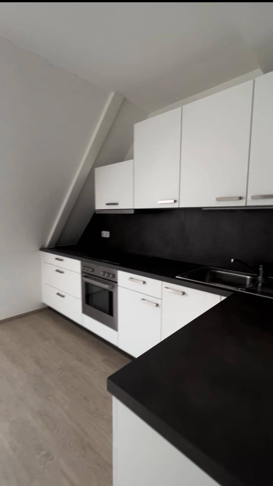 Moderne Küche mit weißen Schränken, schwarzen Arbeitsplatten und integriertem Backofen unter der Dachschräge.