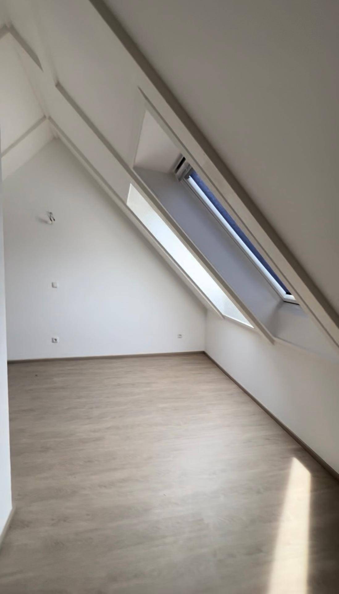 Geräumiger Dachgeschossraum mit schrägen Wänden, hellem Laminatboden und einem großen Dachfenster.