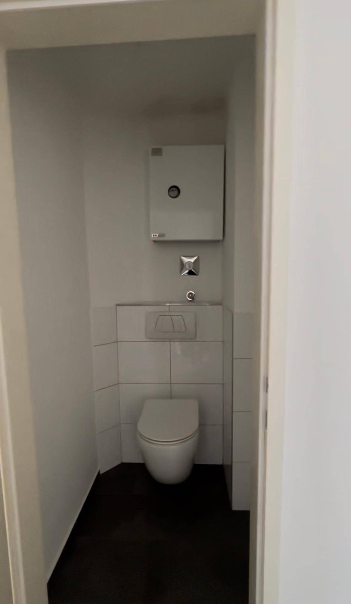 Kompaktes Gäste-WC mit wandhängender Toilette und weißen Fliesen an den Wänden sowie dunklem Boden.