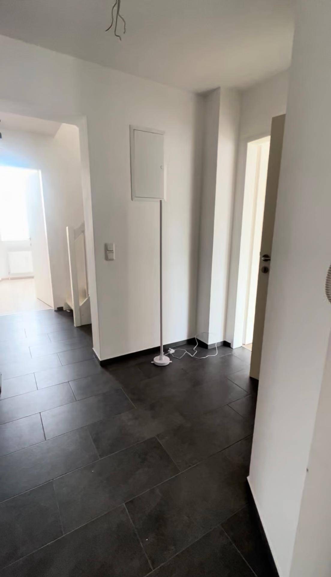 Geräumiger Flur mit dunklem Fliesenboden und weißen Wänden, der zu weiteren Räumen der Wohnung führt.
