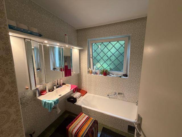 Badezimmer mit Badewanne, Einzelwaschbecken, Spiegelschrank und Fenster.
