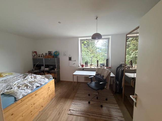 Geräumiges Schlafzimmer mit Holzbett, Schreibtisch und großem Fenster mit Waldblick.