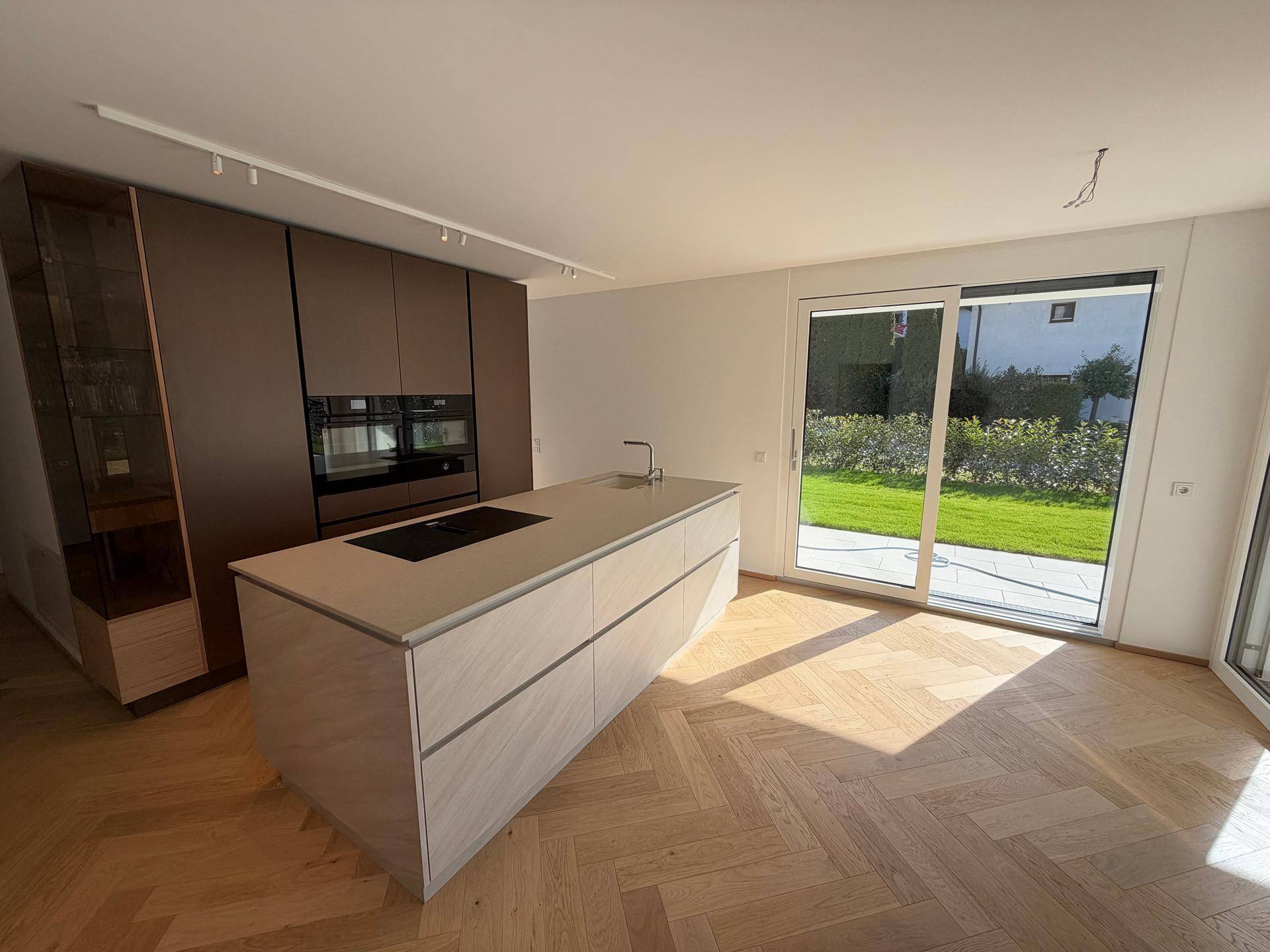Moderne Einbauküche mit integrierten Geräten, Kücheninsel und direktem Zugang zum Garten.