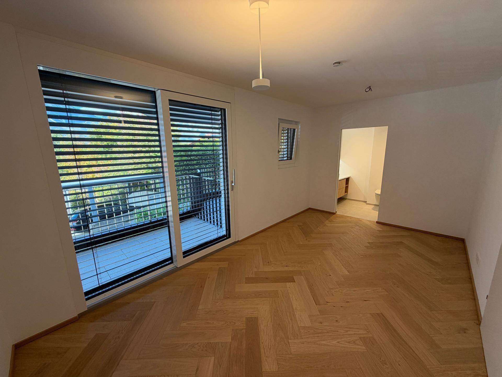 Helles Schlafzimmer mit Fischgrätparkett und direktem Zugang zu einem Balkon.