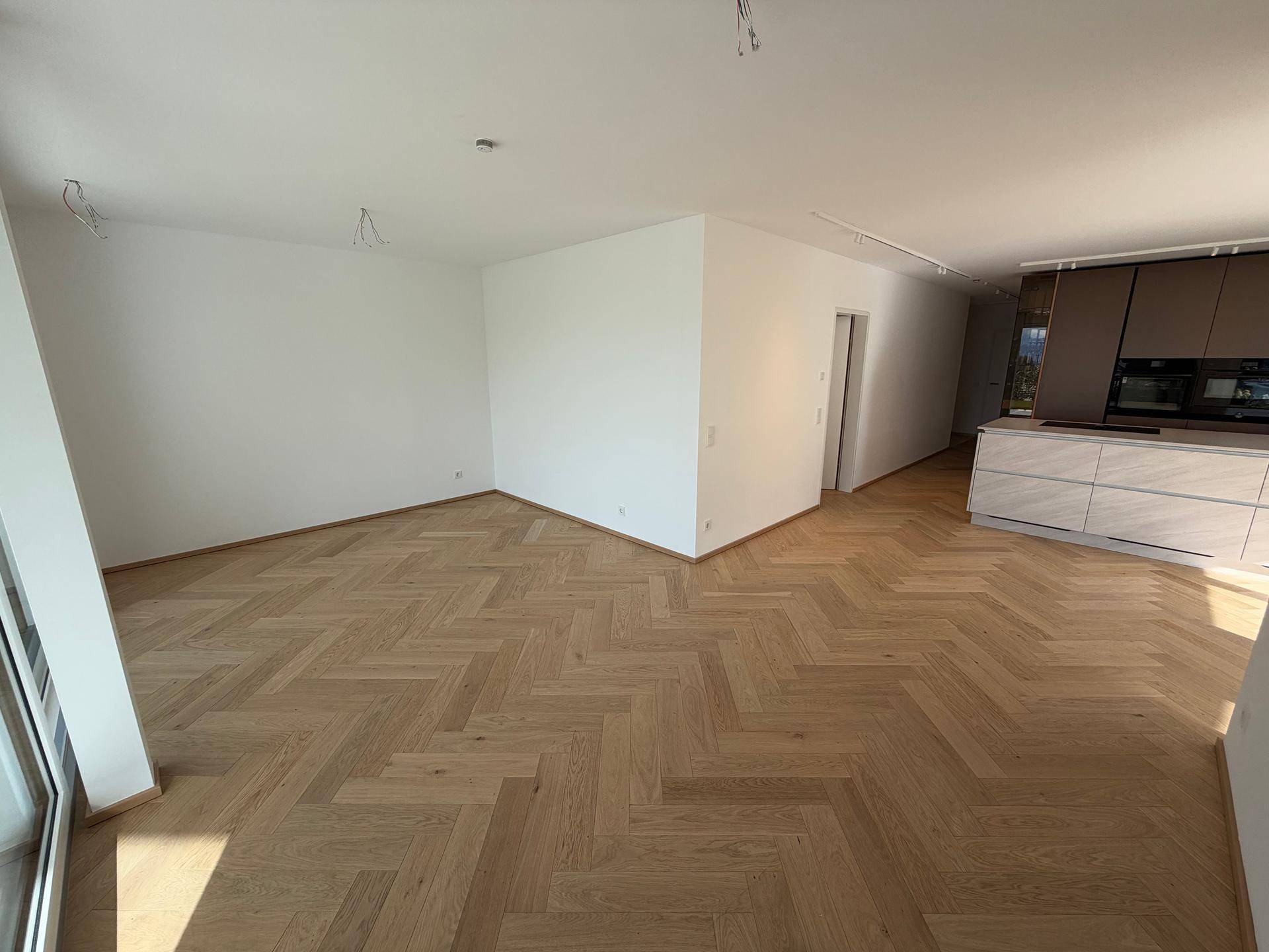 Geräumiger, offener Wohnbereich mit elegantem Fischgrätparkett und viel Tageslicht.
