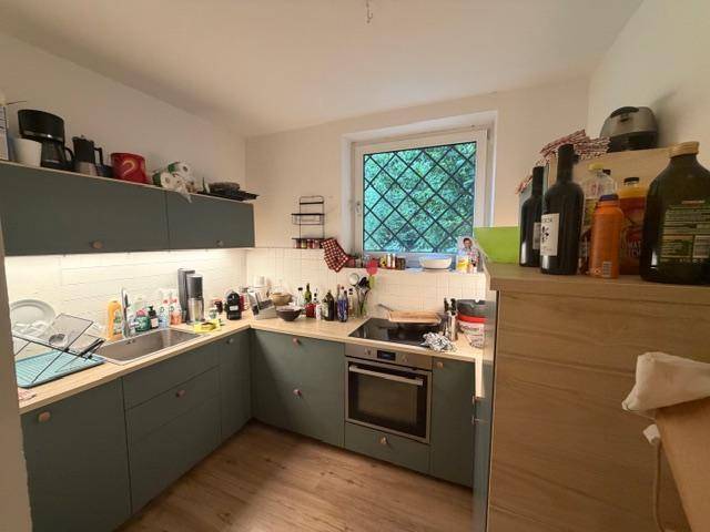 Küche mit blaugrauen Einbauschränken, integriertem Backofen und Fenster.