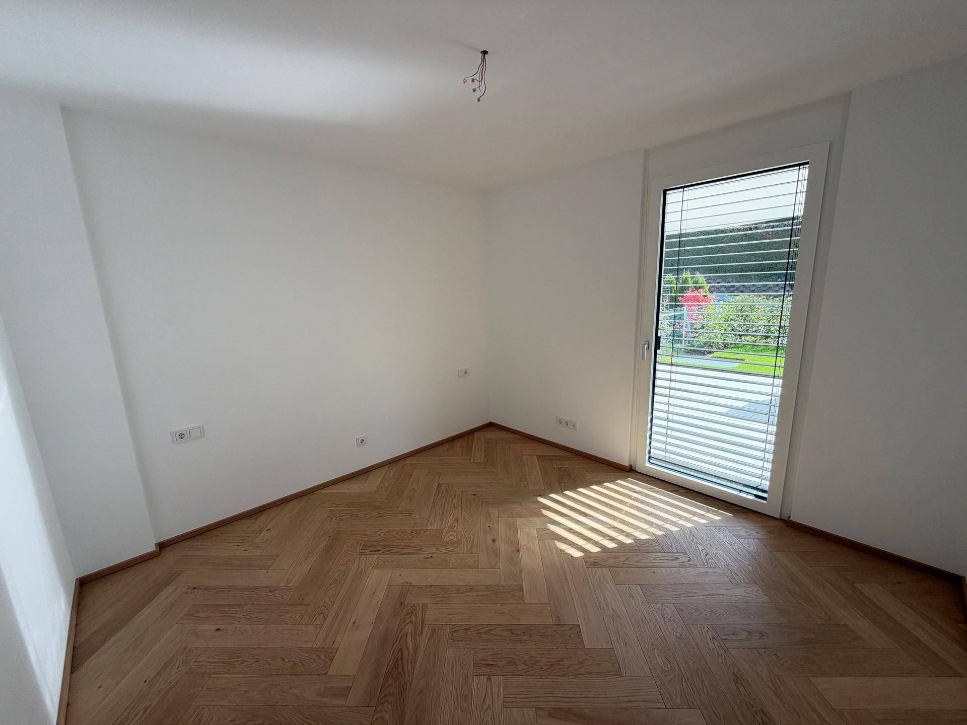 Helles Zimmer mit Fischgrätparkett und Zugang zu einem Außenbereich, ideal als Schlaf- oder Arbeitszimmer.