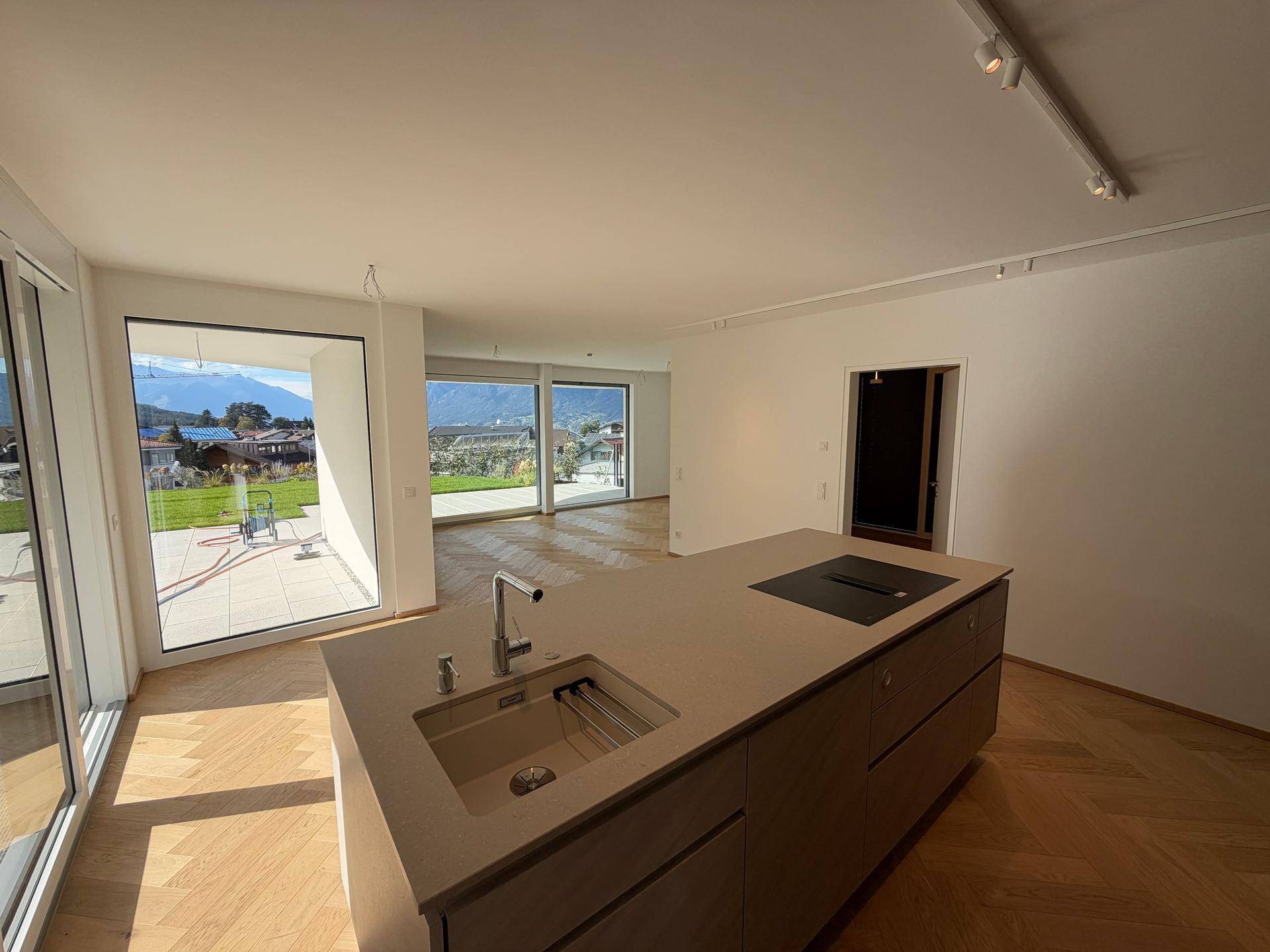 Helle, offene Küche mit moderner Kücheninsel, Parkettboden und großen Fenstern mit Bergblick.