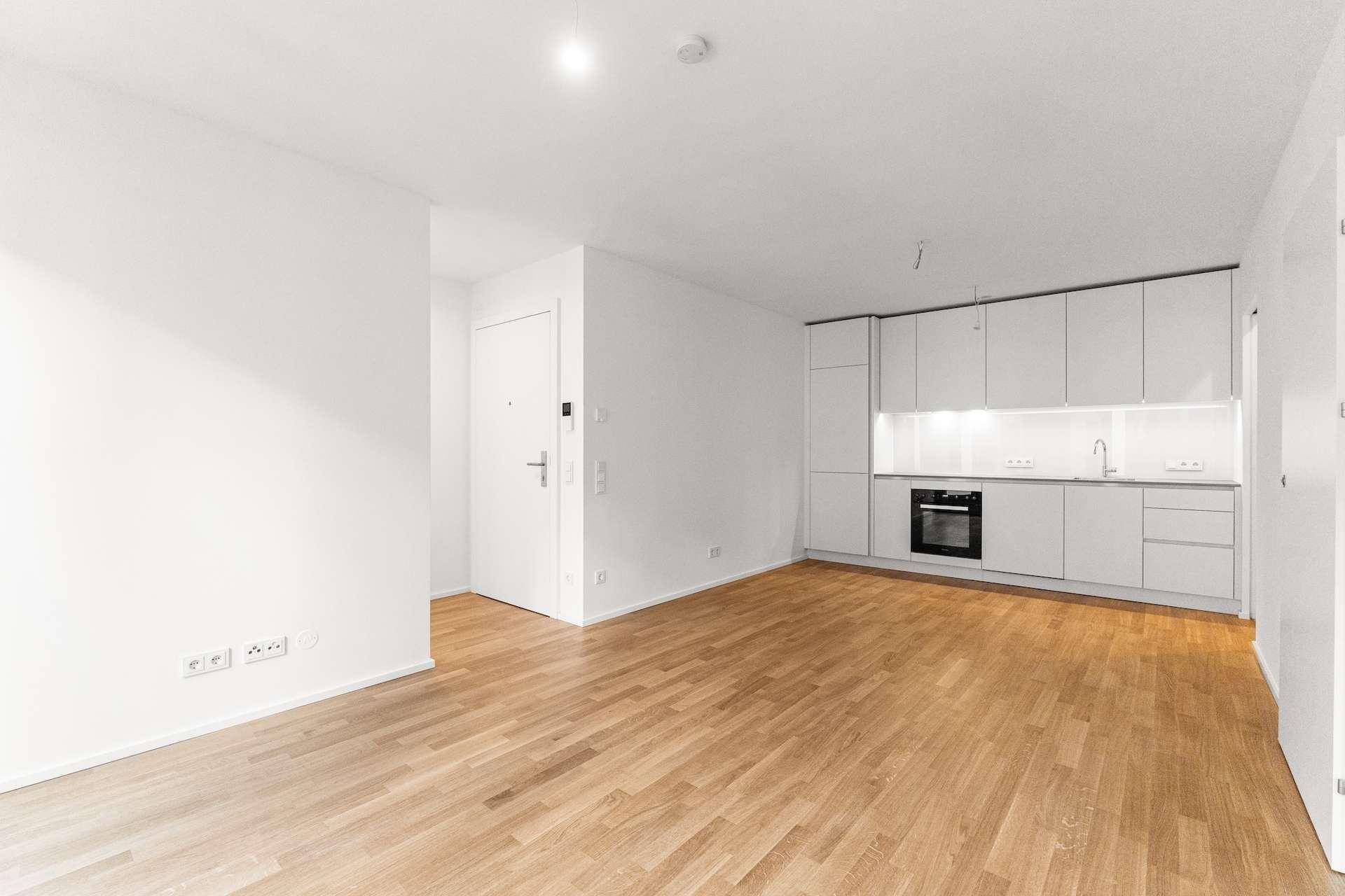 Moderner Wohnbereich mit integrierter weißer Küche und Holzboden, ideal für offenes Wohnen.