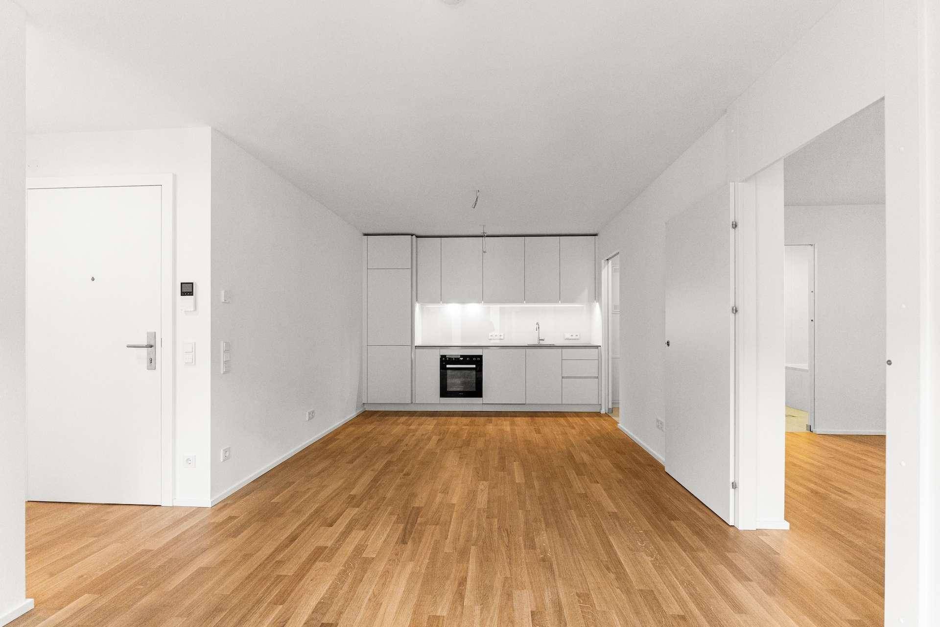 Geräumiger Wohnbereich mit integrierter, minimalistischer Küche und warmem Holzboden.