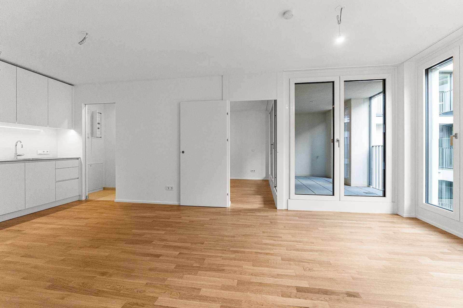 Heller Wohnbereich mit integrierter Küche und Holzboden, mit Zugang zu einem Außenbereich.