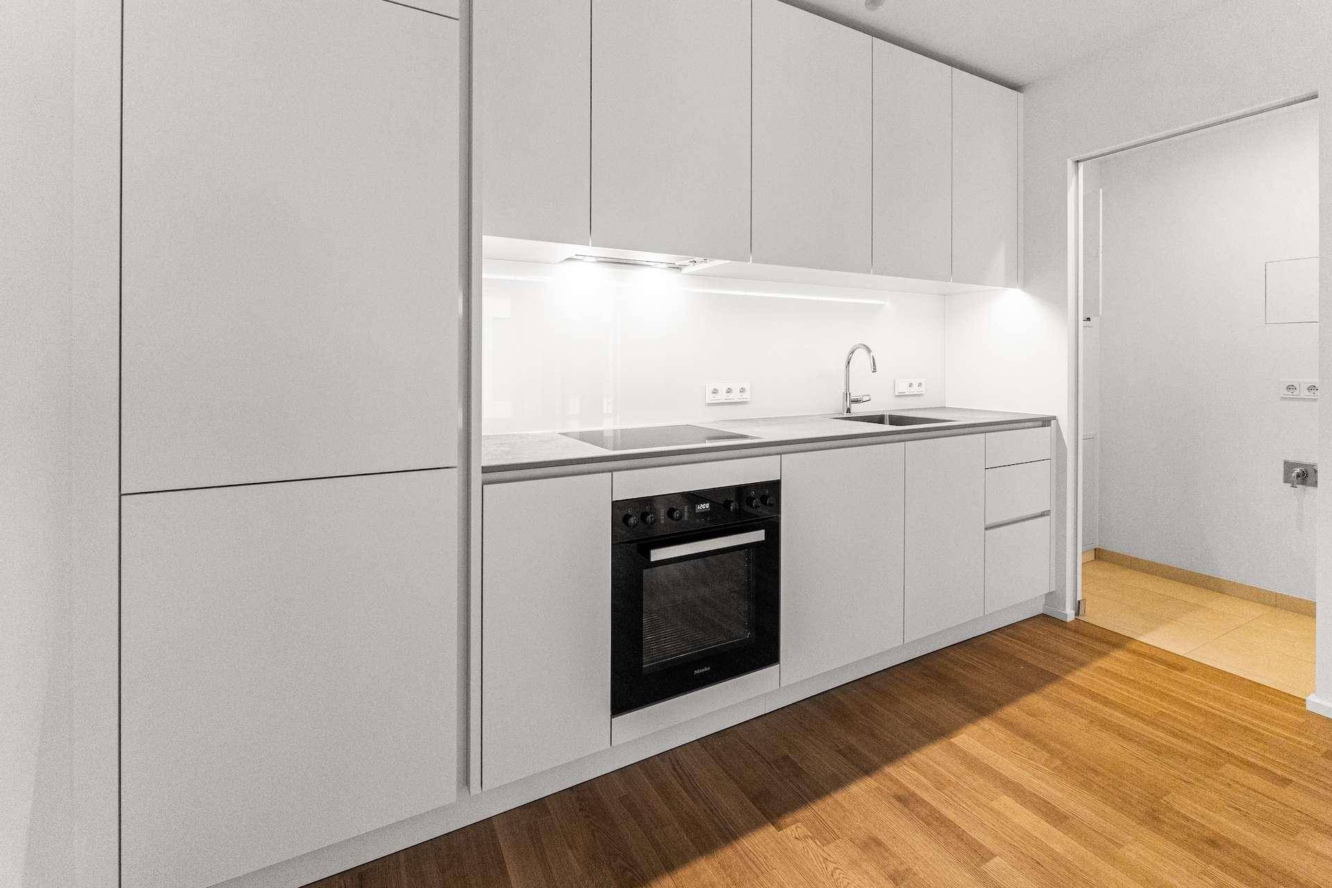 Moderne Einbauküche mit weißen Schränken, integriertem Backofen und heller Arbeitsplatte.