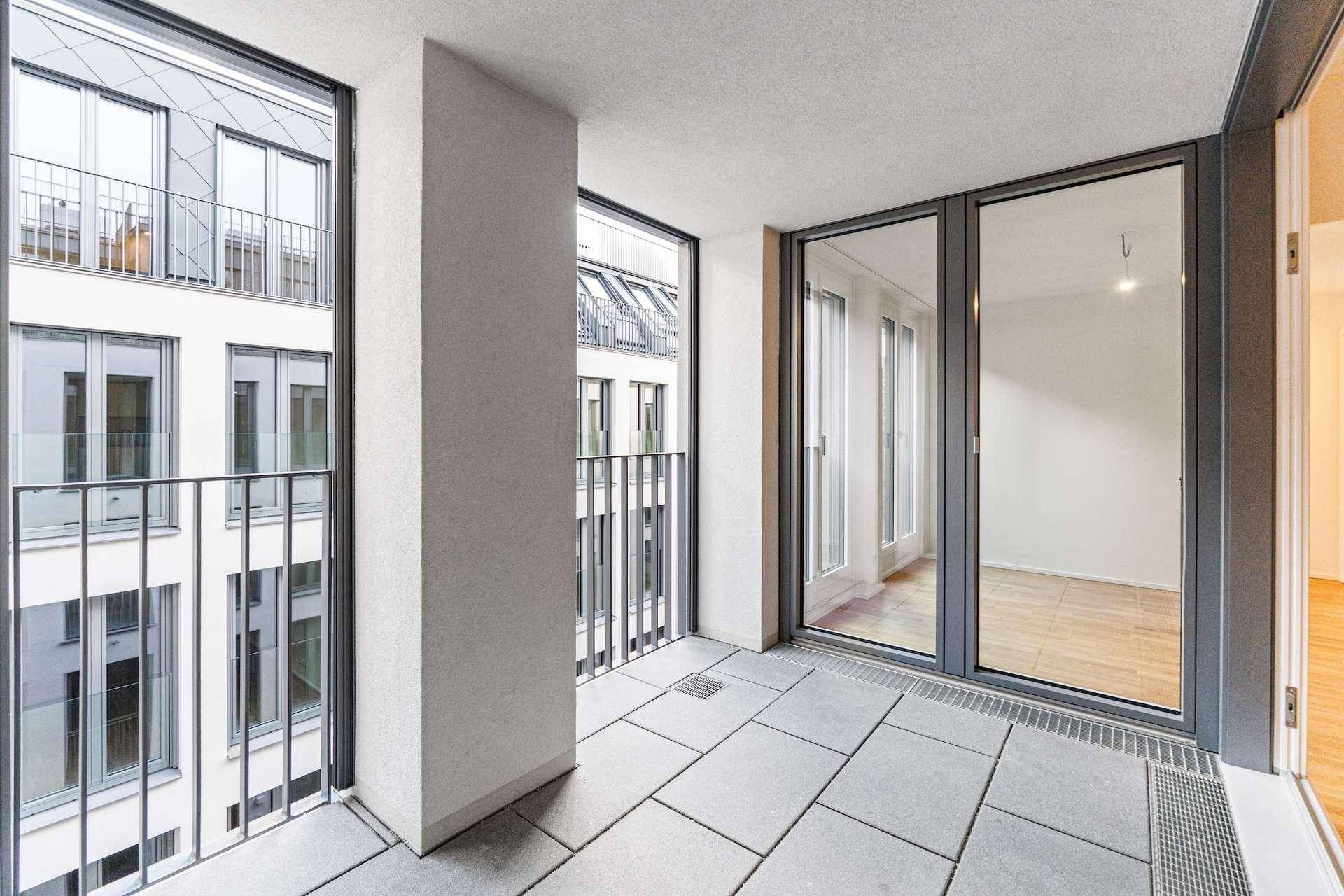 Geräumige Loggia mit Fliesenboden und Blick auf den Innenhof des modernen Gebäudes.