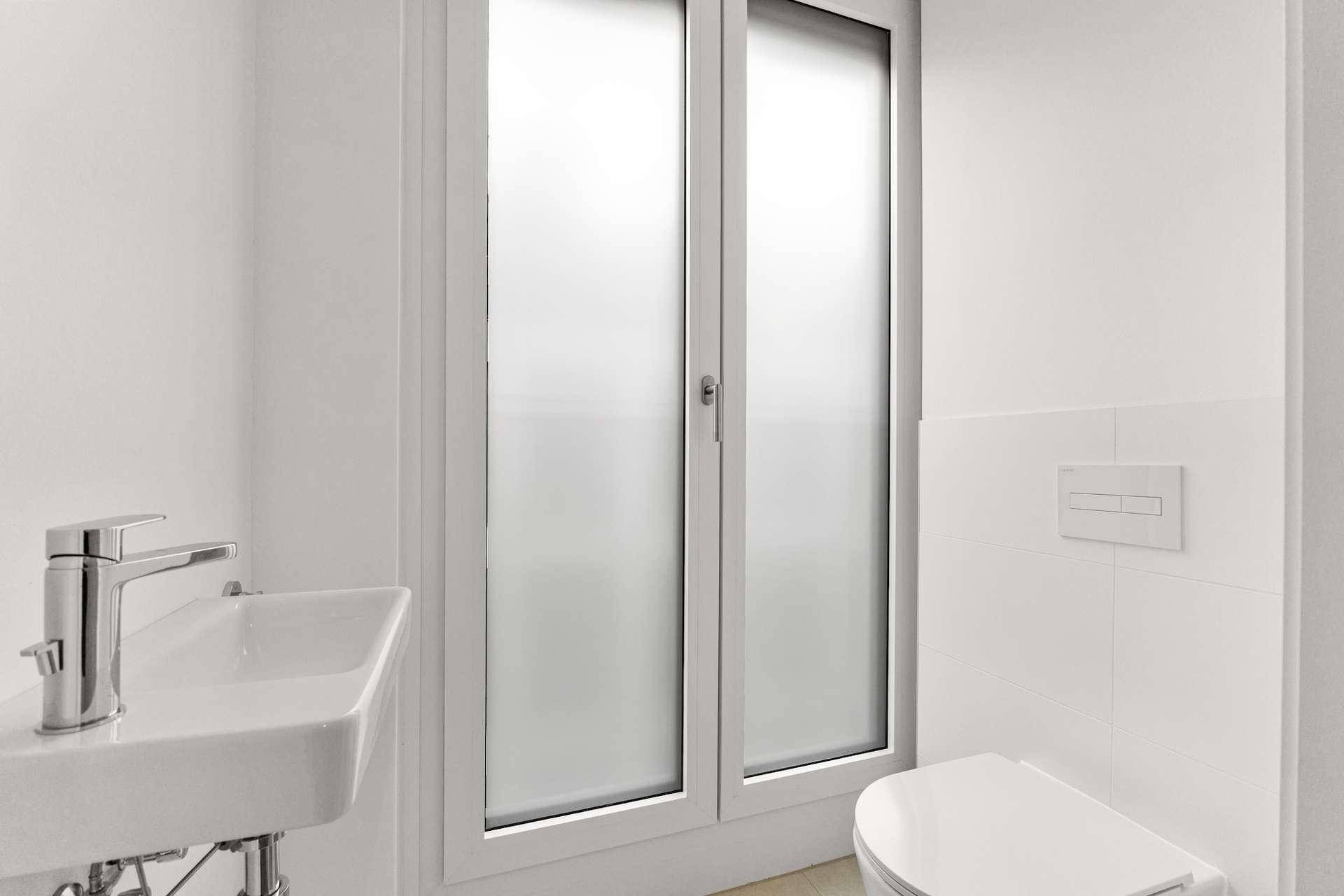 Modernes Gäste-WC mit wandhängender Toilette, kleinem Waschbecken und Milchglasfenster.