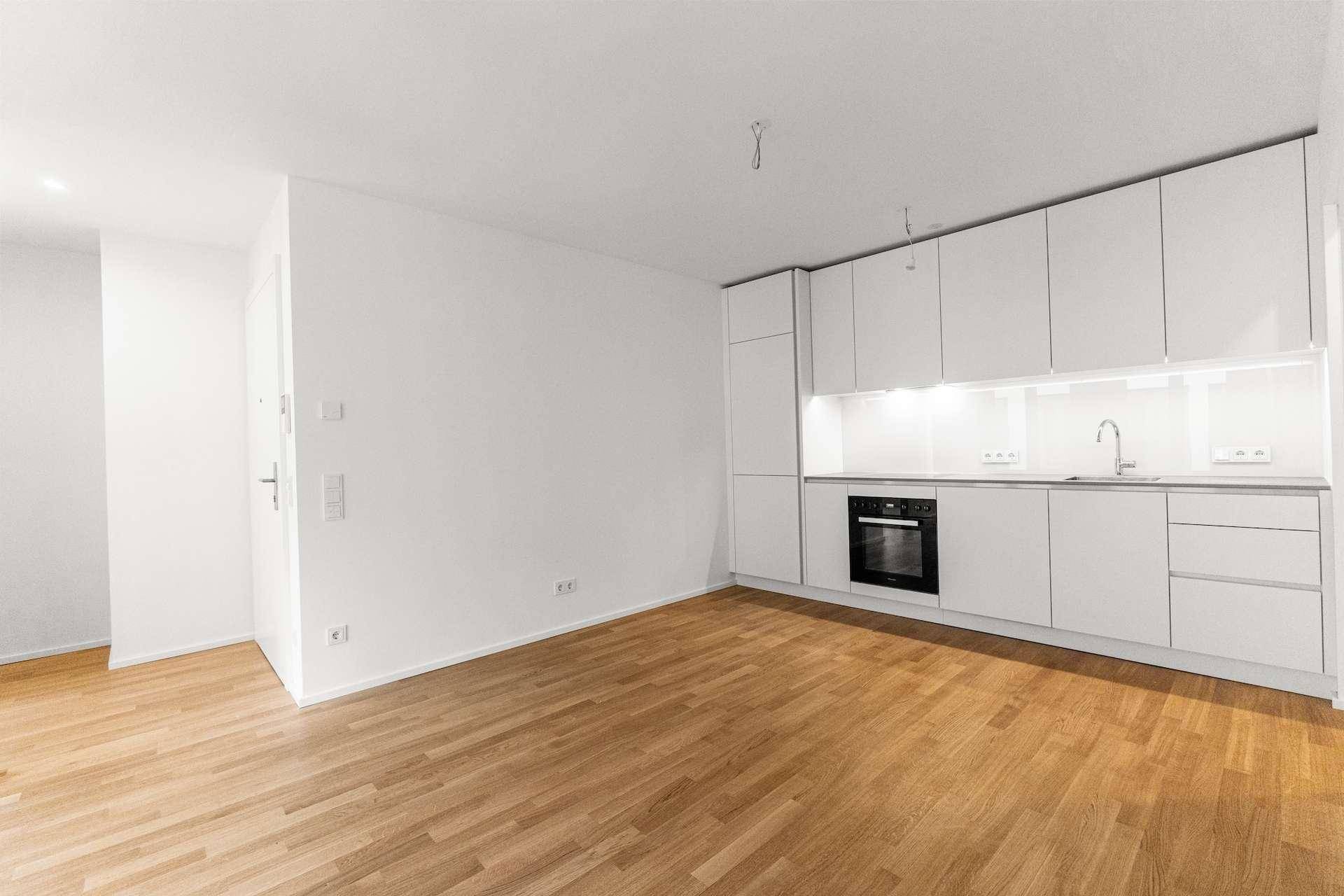 Offener Wohnbereich mit integrierter weißer Küche und Holzboden, ideal für modernes Wohnen.