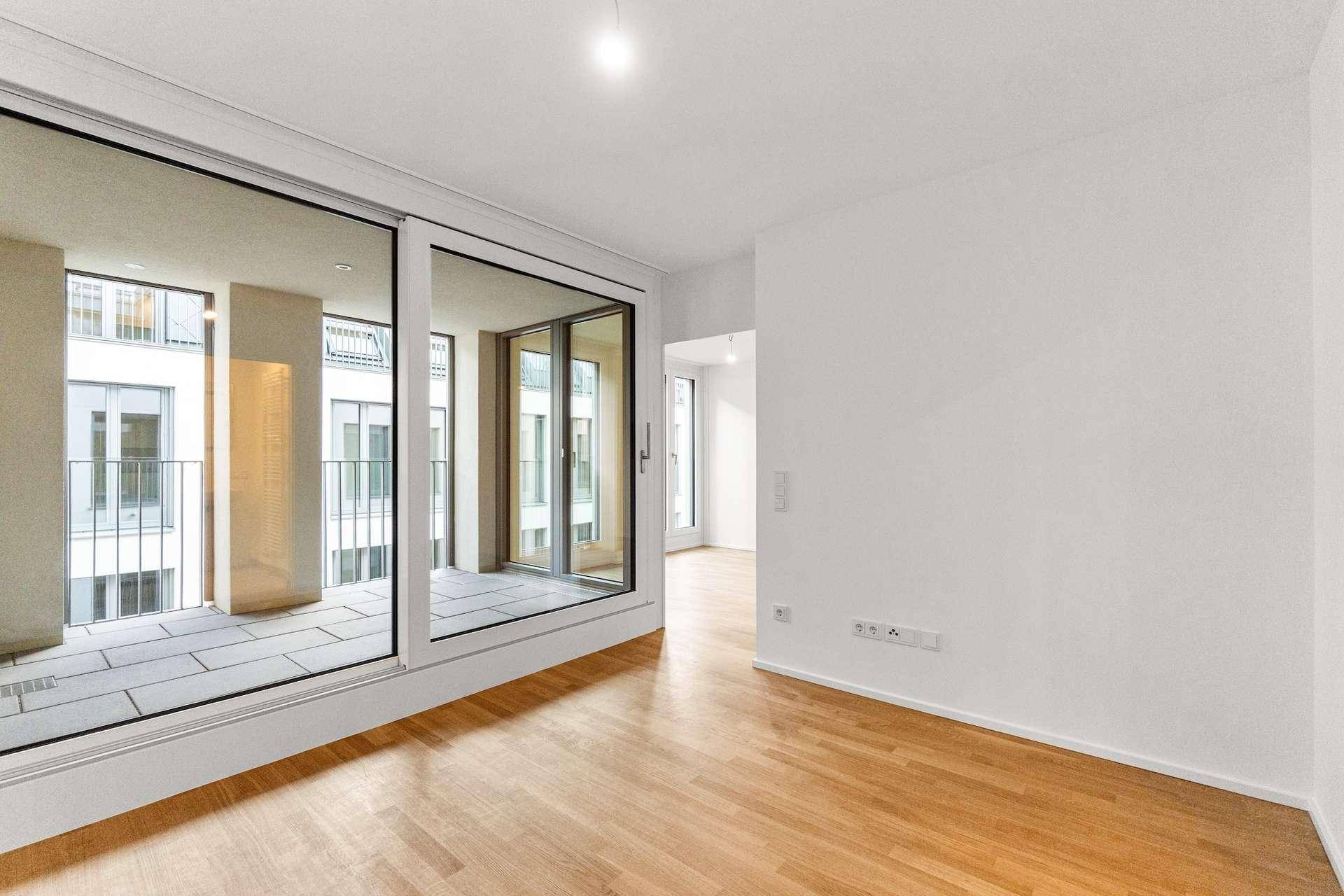 Heller Wohnraum mit Holzboden und Zugang zu einer gefliesten Loggia oder Terrasse.