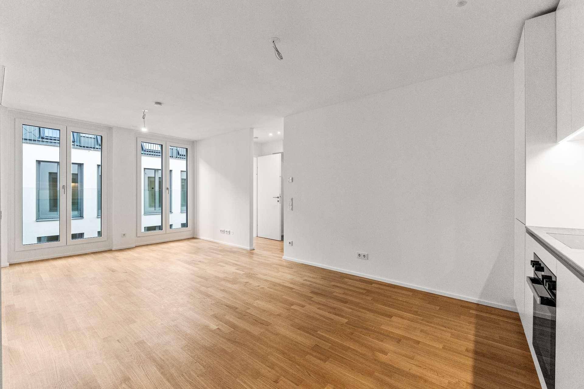 Geräumiger Wohnbereich mit Holzboden und großen Fenstern, die auf den Innenhof blicken.