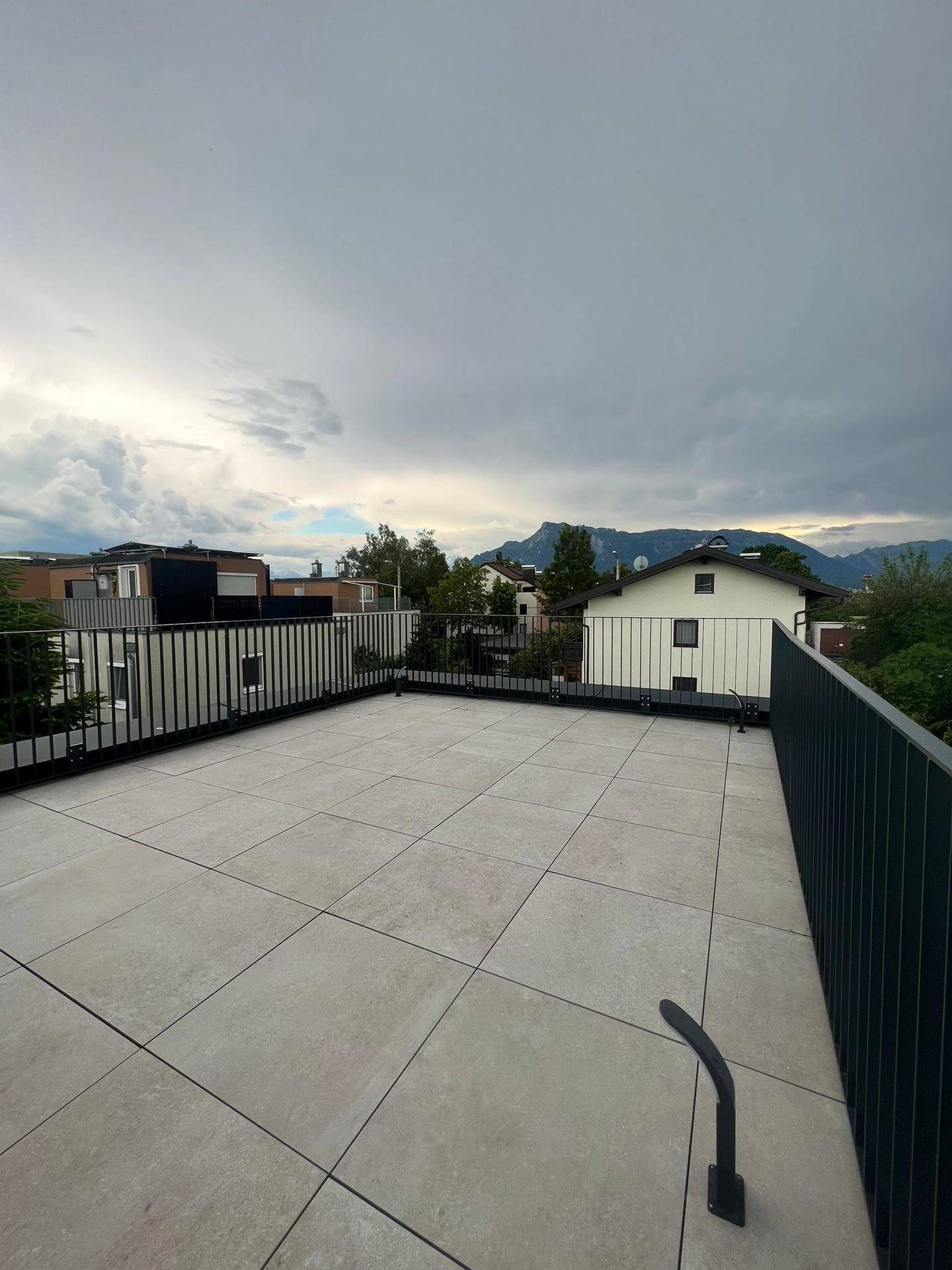Große Dachterrasse mit Fliesen und Metallgeländer, bietet weite Aussicht auf die Umgebung.