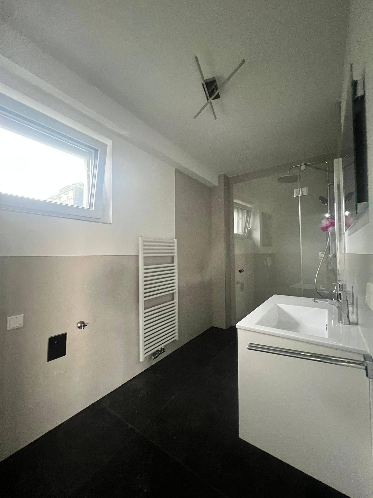 Modernes Badezimmer mit Dusche, Waschbecken, beheiztem Handtuchhalter und Fenster.