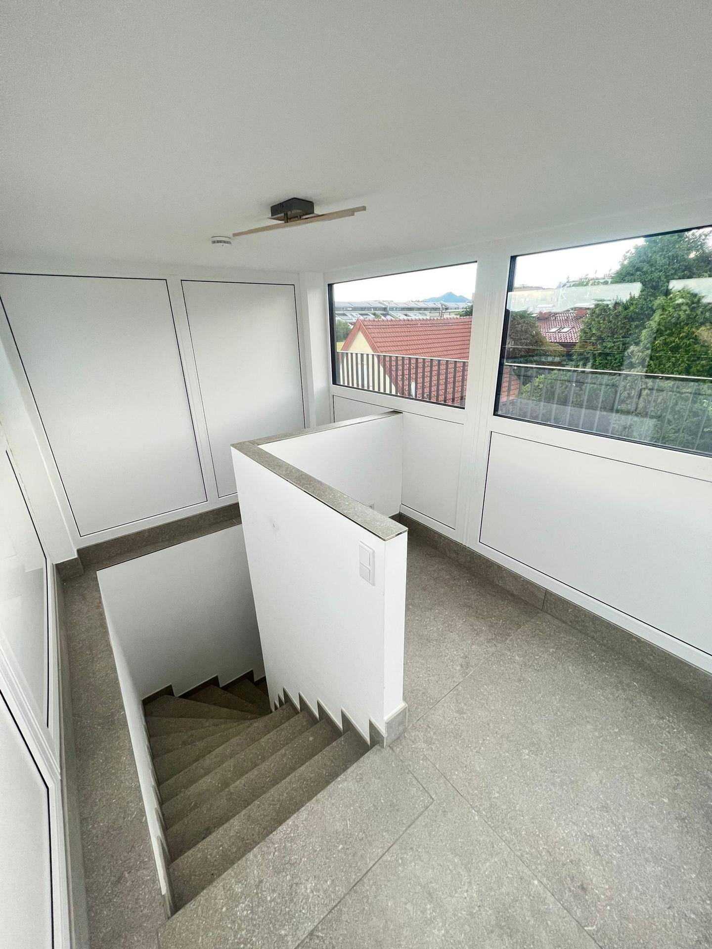 Heller Treppenabsatz mit großen Fenstern und Zugang zur Dachterrasse.
