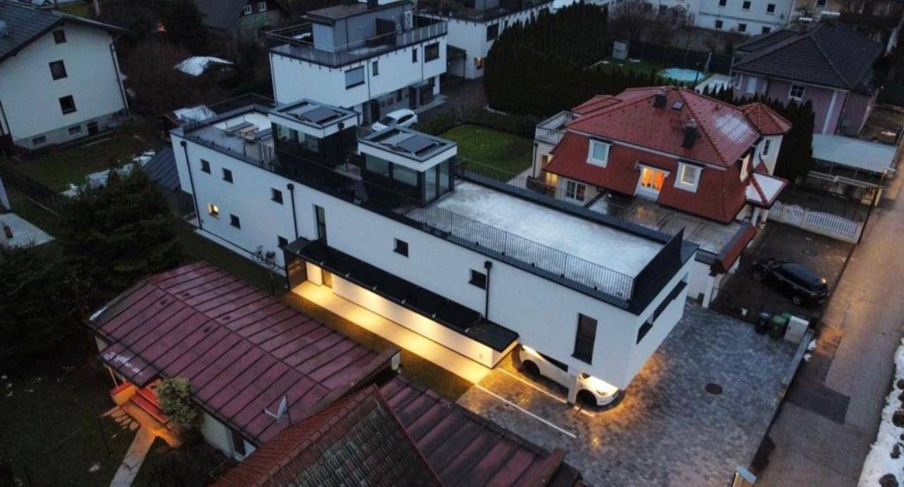 Moderne Architektur mit Flachdach und großen Fenstern, umgeben von Wohngebäuden.
