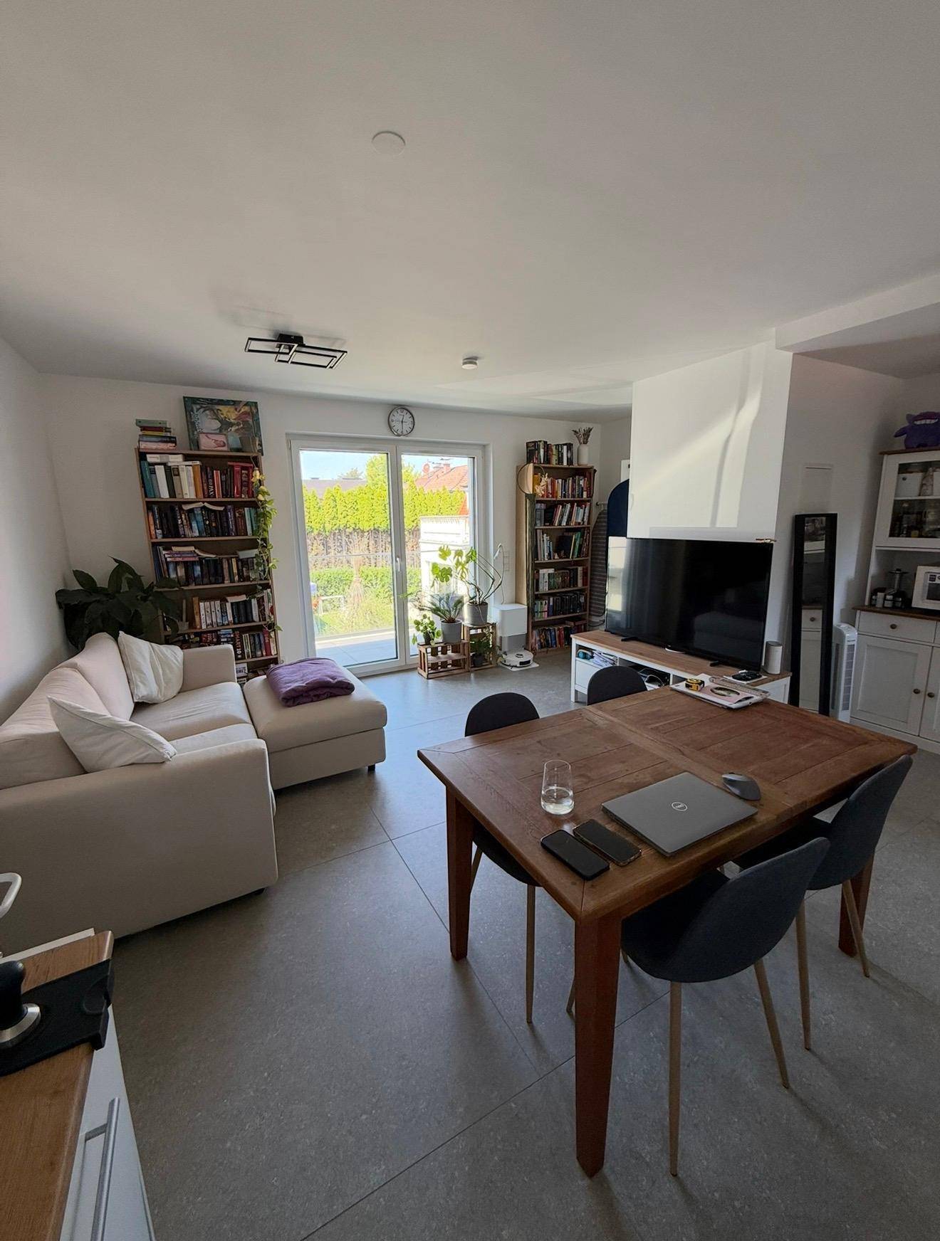 Heller Wohn- und Essbereich mit Sofa, Bücherregalen und Zugang zum Garten.