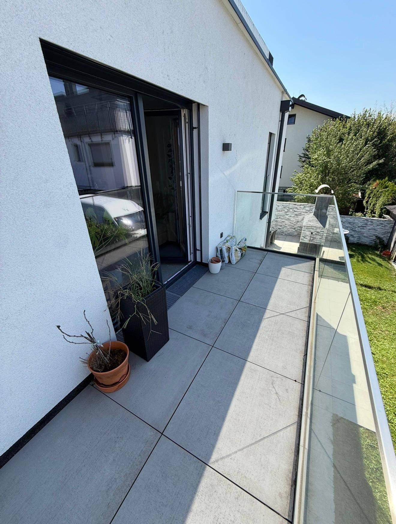 Heller Balkon mit Fliesenboden, Glasgeländer und Blick auf die Umgebung.