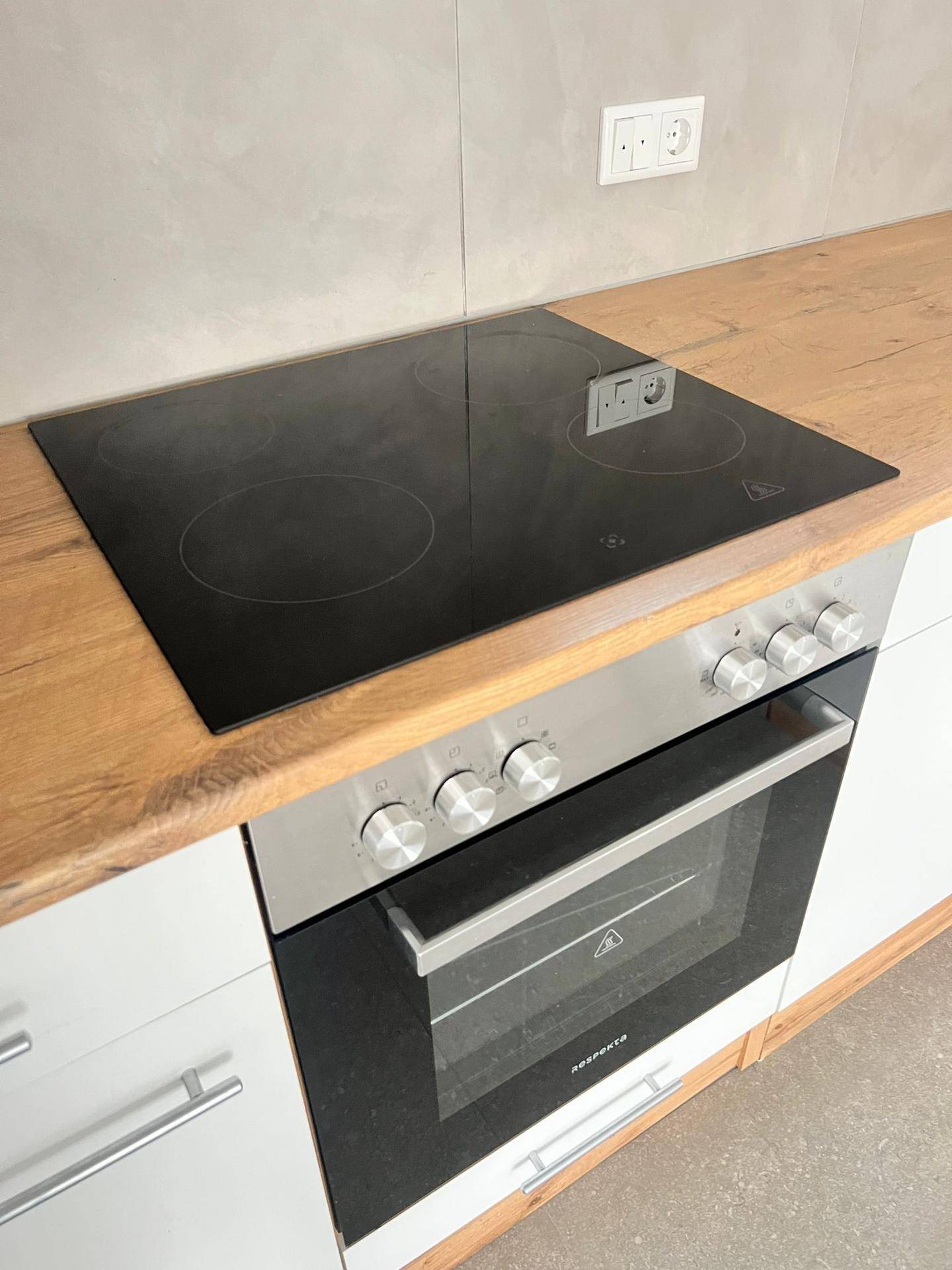 Moderne Küche mit Induktionskochfeld, Backofen und Arbeitsplatte in Holzoptik.
