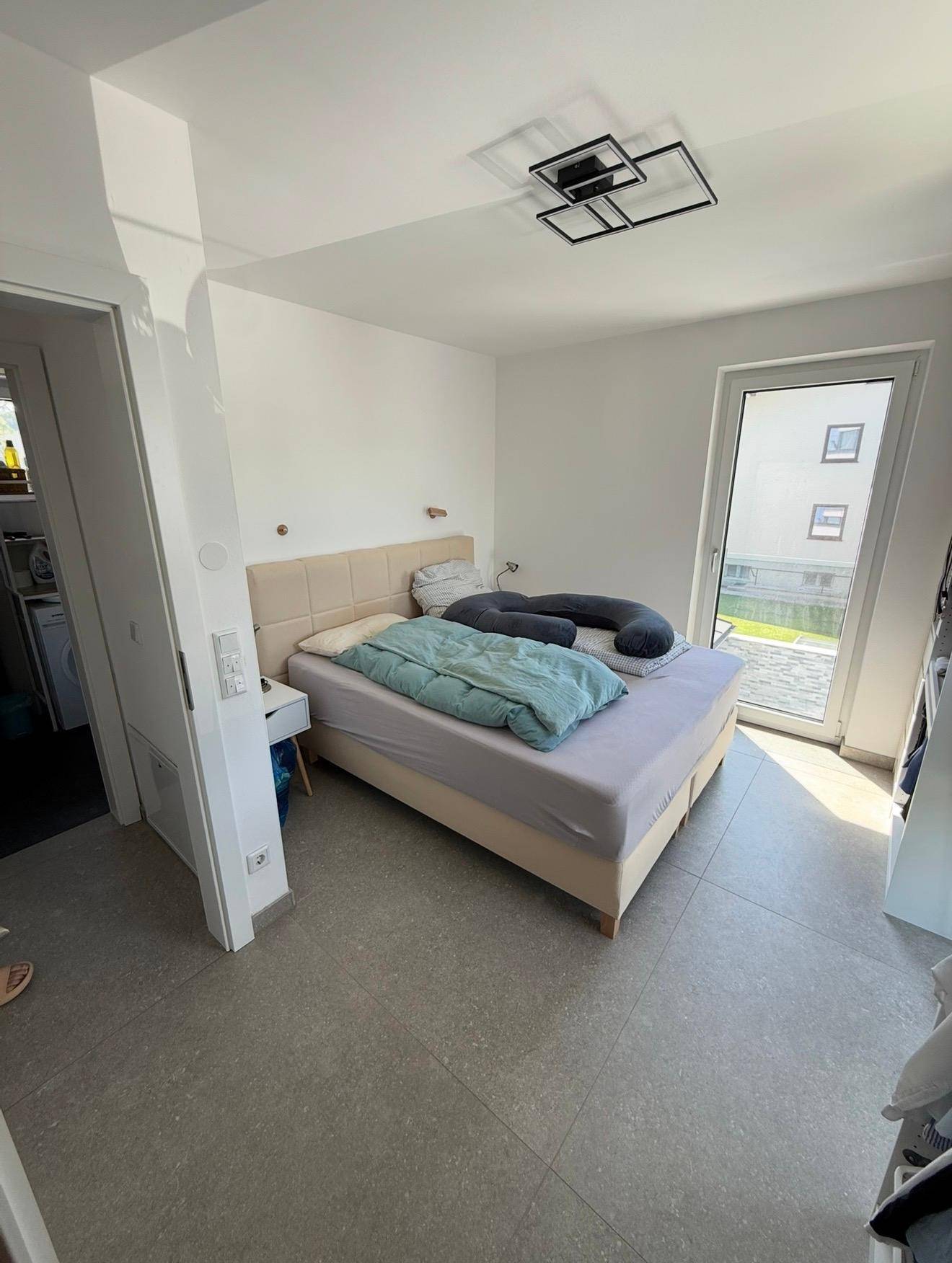 Schlafzimmer mit Doppelbett, hellem Fliesenboden und Zugang zu einem Außenbereich.