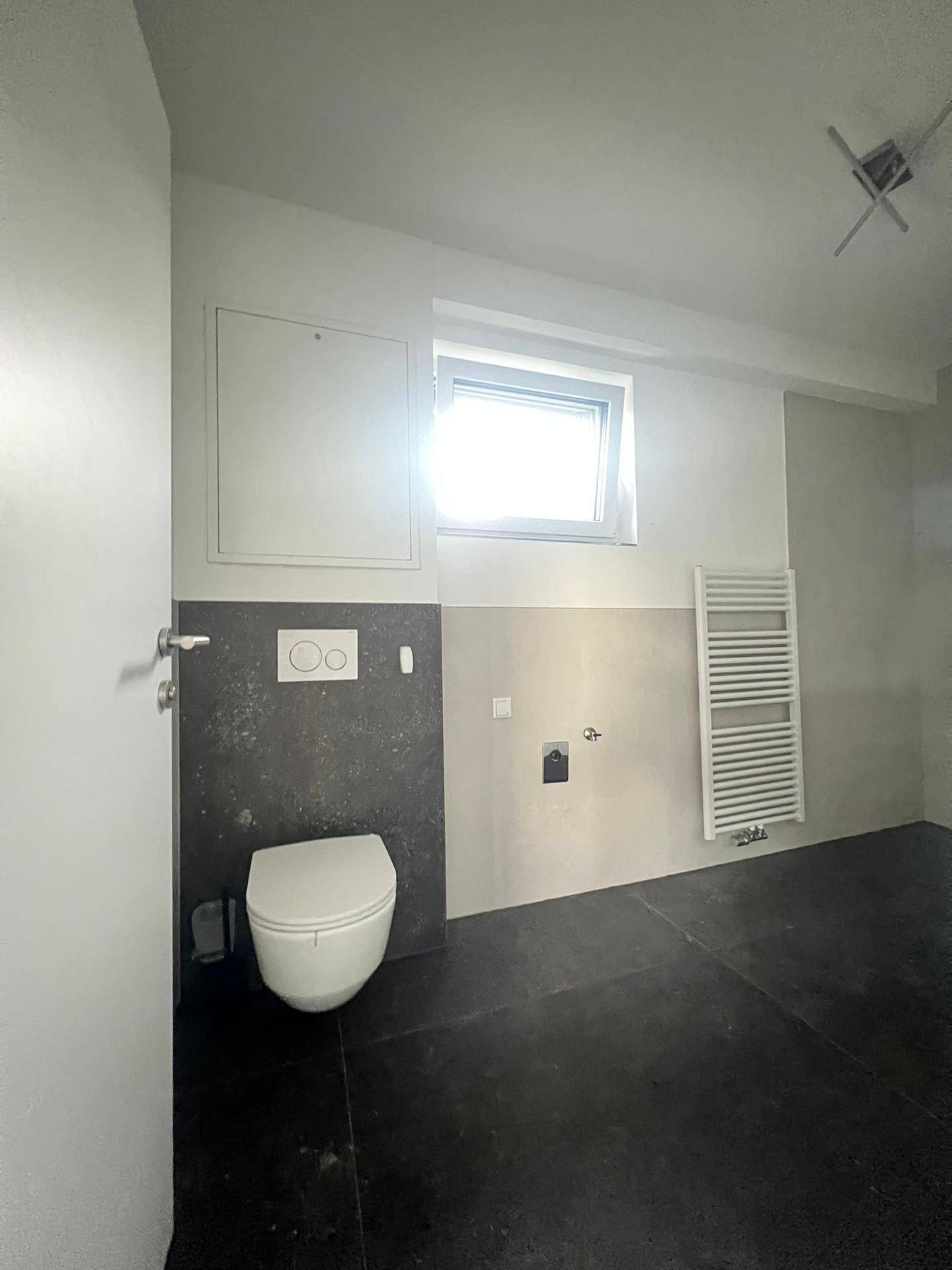 Modernes Badezimmer mit wandhängendem WC, beheiztem Handtuchhalter und Fenster.