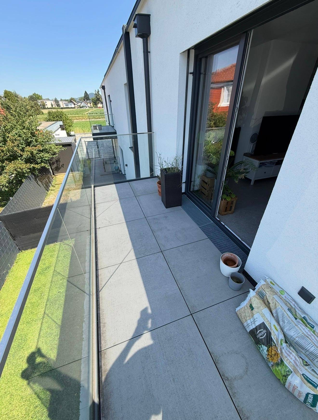 Geräumiger Balkon mit Fliesenboden und Glasgeländer, bietet Blick ins Grüne.