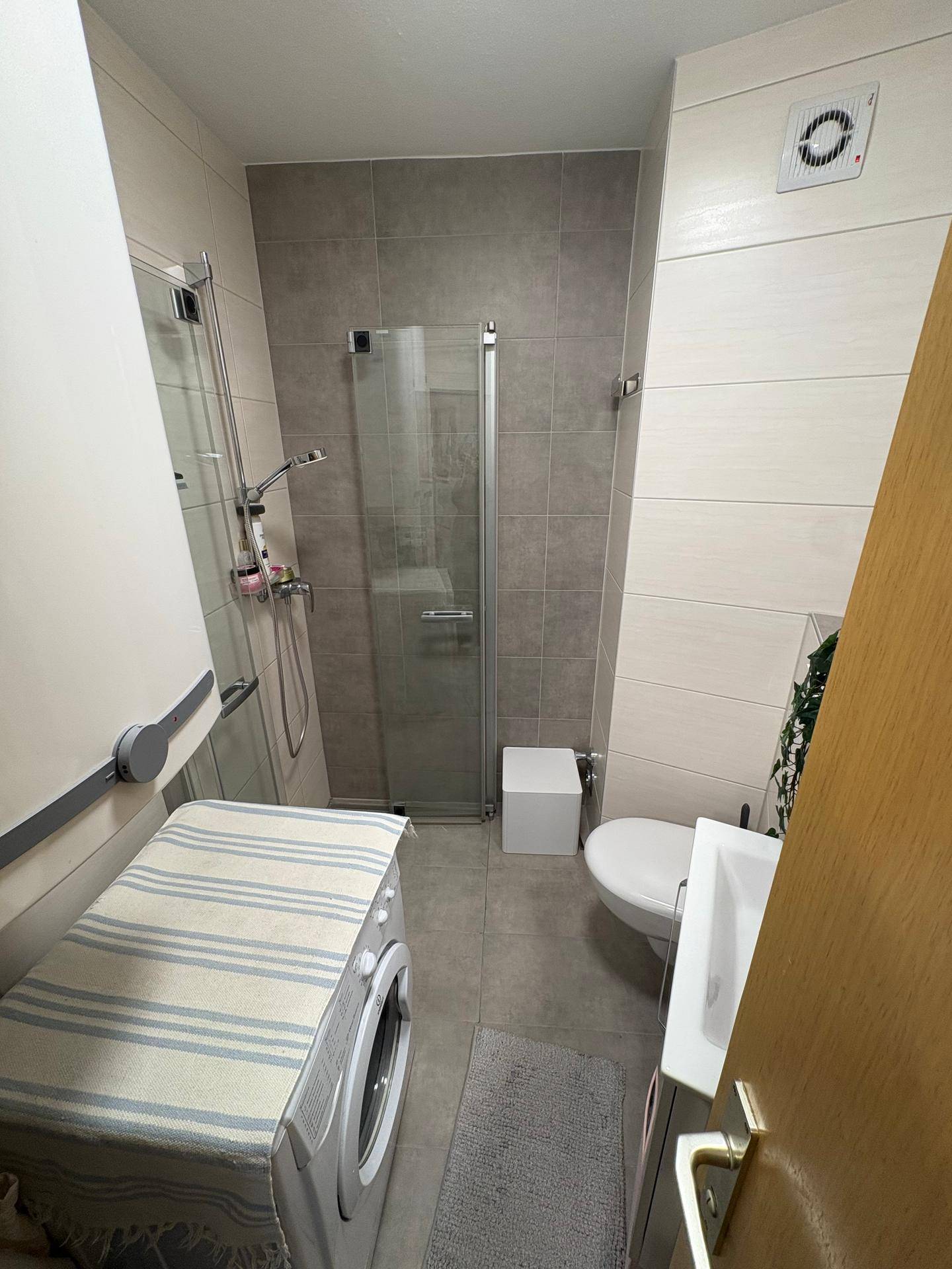 Modernes Badezimmer mit Dusche, WC, Waschbecken und integrierter Waschmaschine.