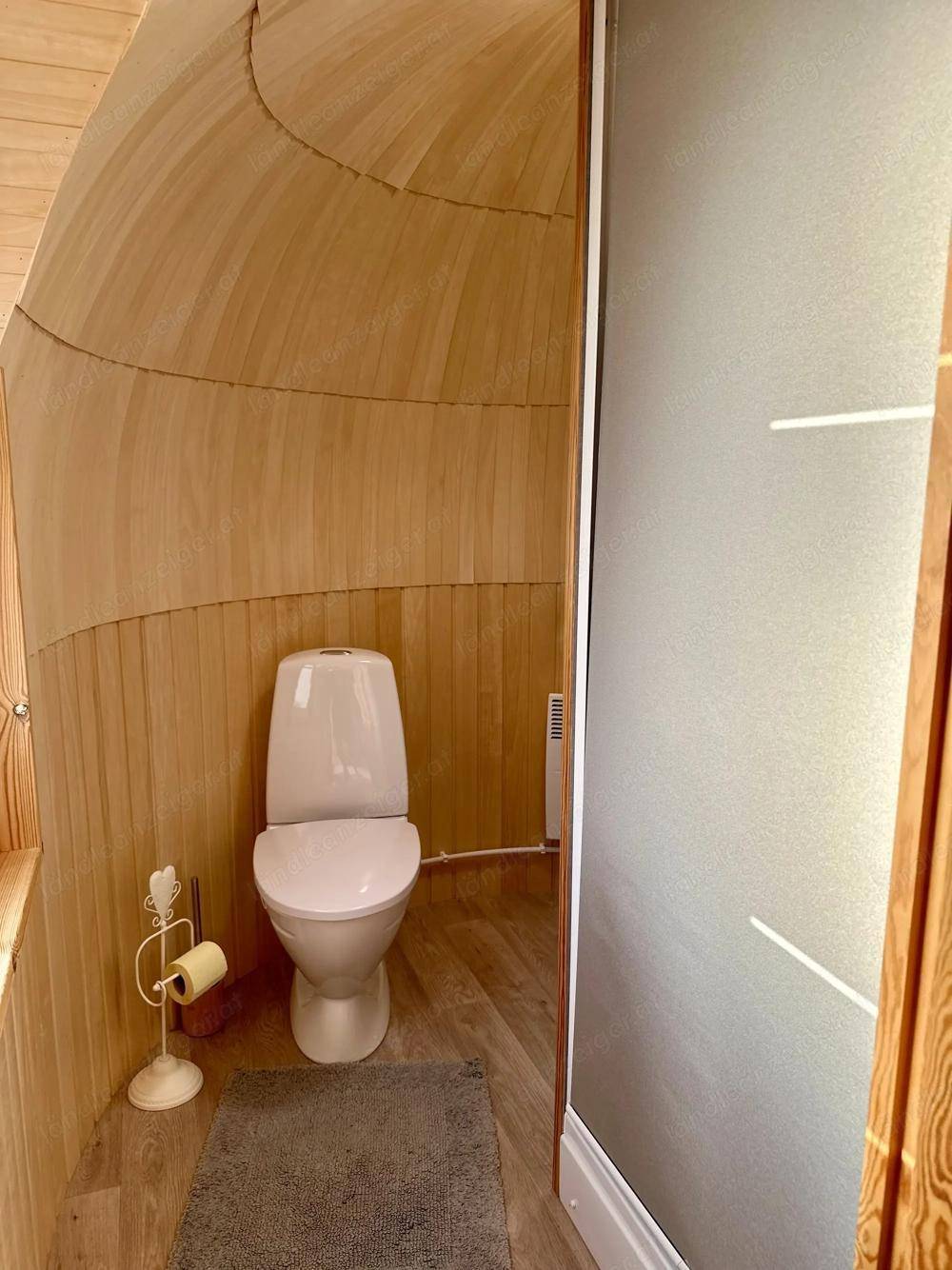 Schlichtes WC mit weißer Toilette und Holzverkleidung an den gewölbten Wänden.