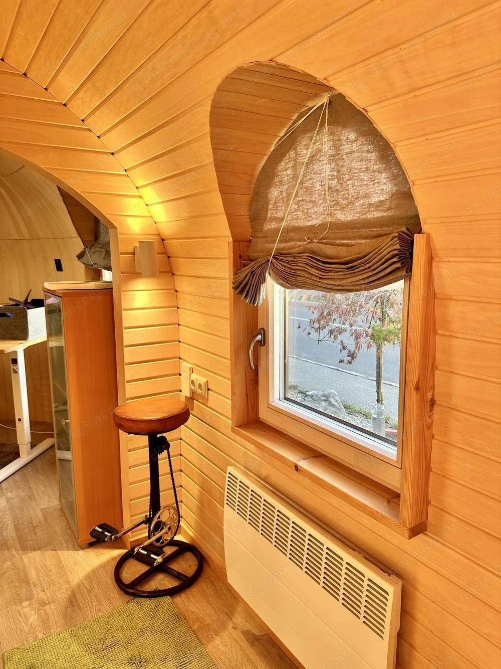 Detailansicht eines runden Fensters mit Rollo und Heizkörper in einem Raum mit Holzverkleidung.