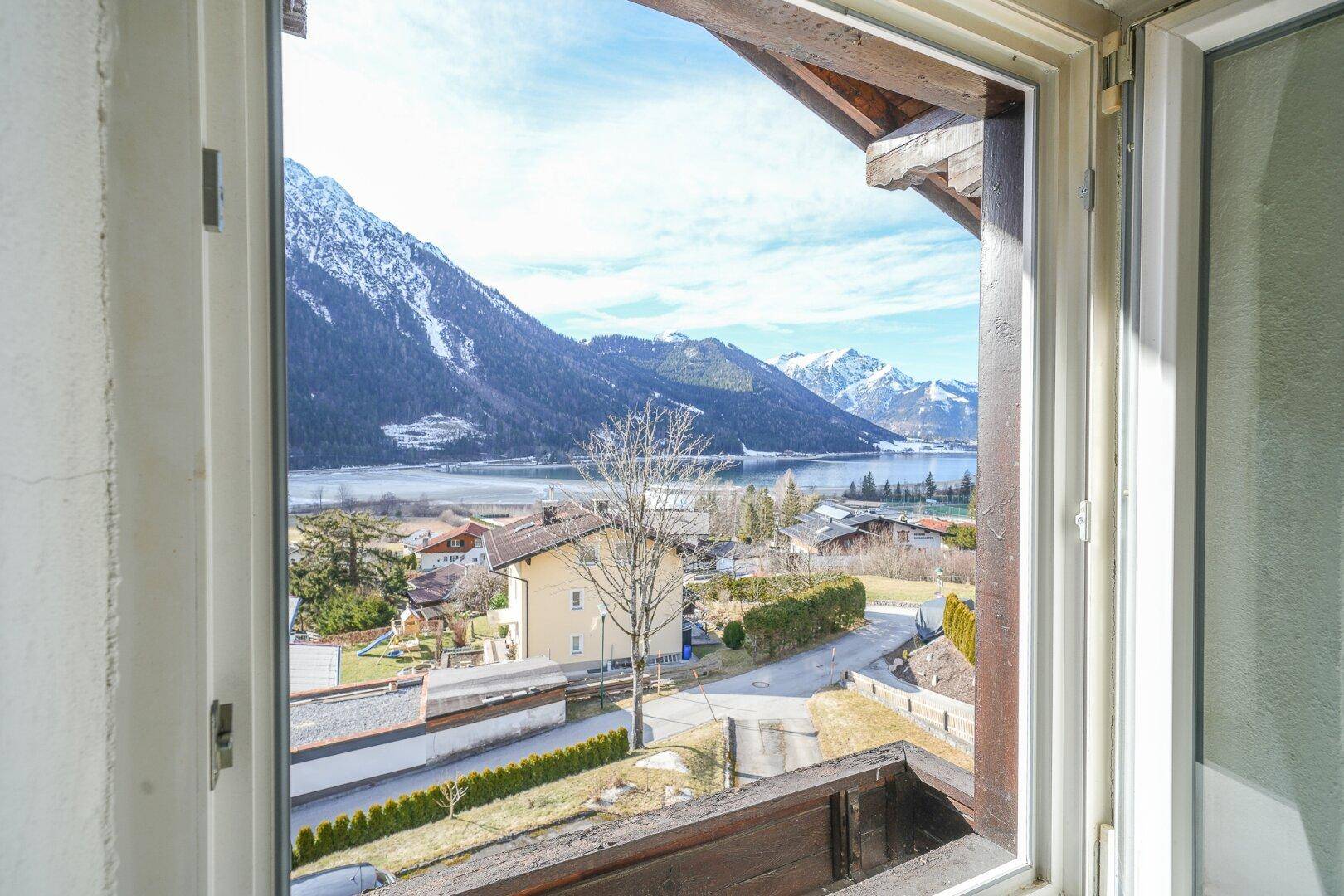 Blick aus einem Fenster auf einen See und die umliegende Berglandschaft.