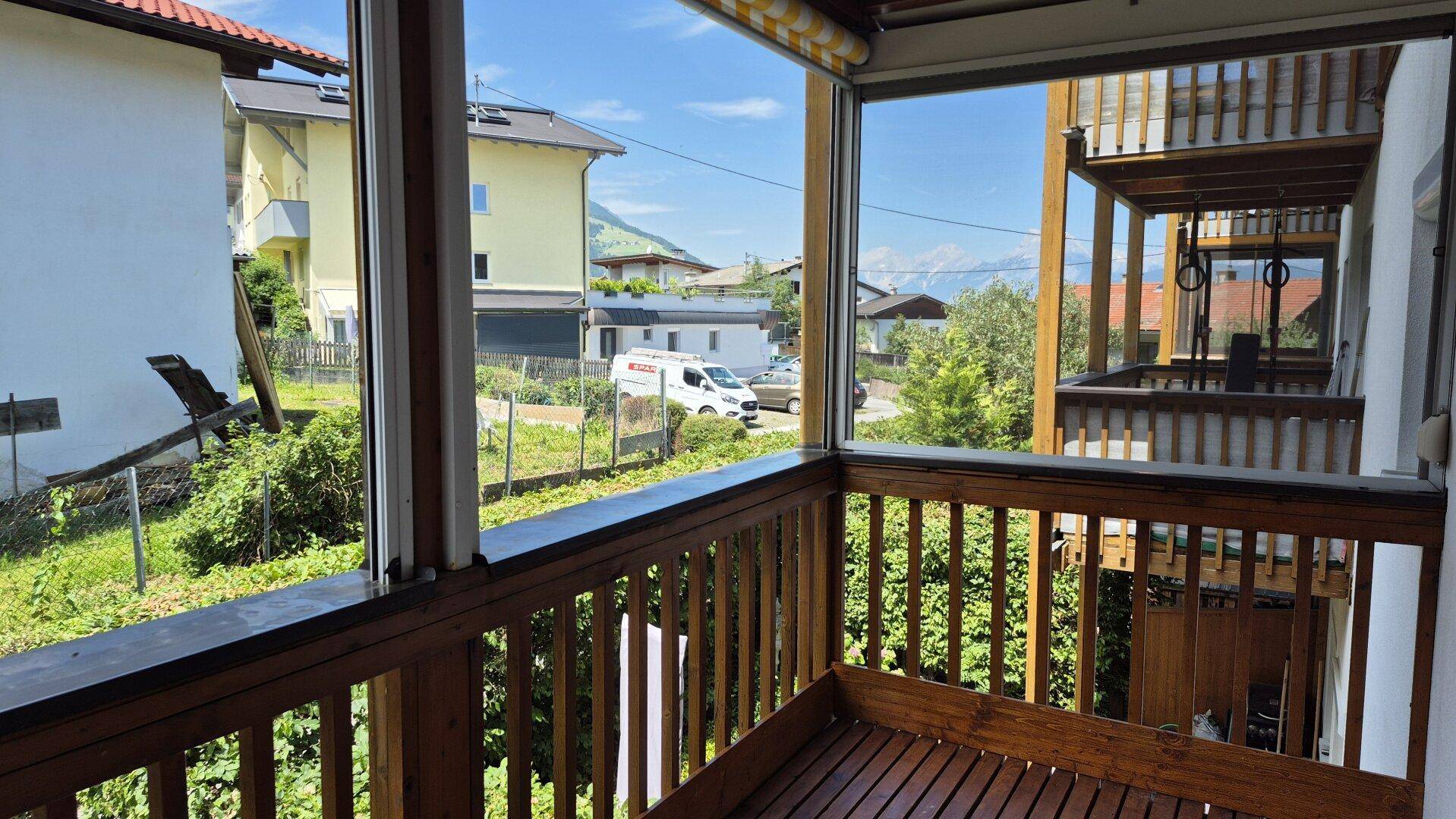 Verglaster Balkon mit Holzboden und Geländer, bietet einen weiten Blick auf die Umgebung und Berge.
