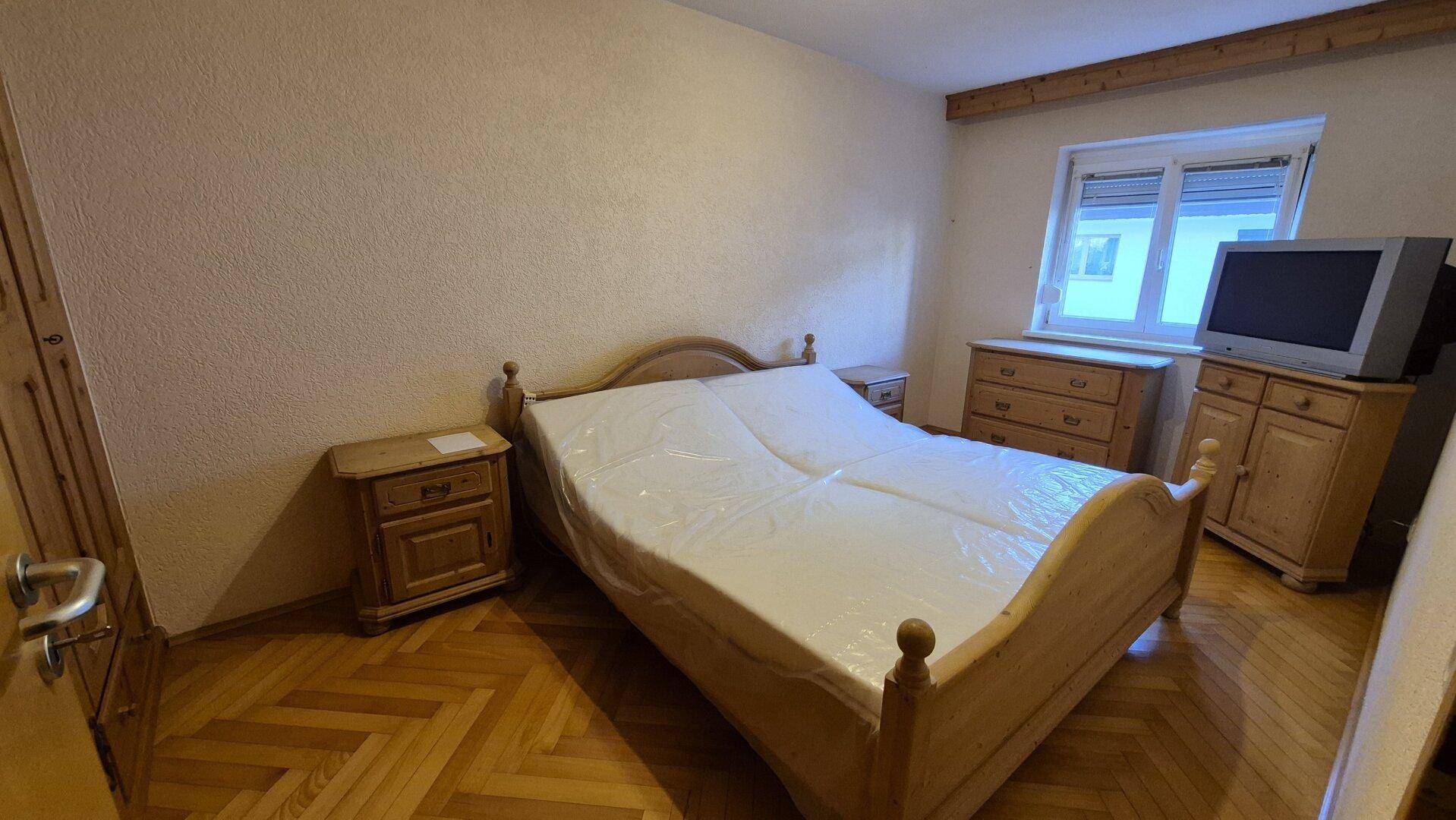 Schlafzimmer mit Holzparkett, traditionellem Holzbett und Nachttischen, sowie einem Fenster.