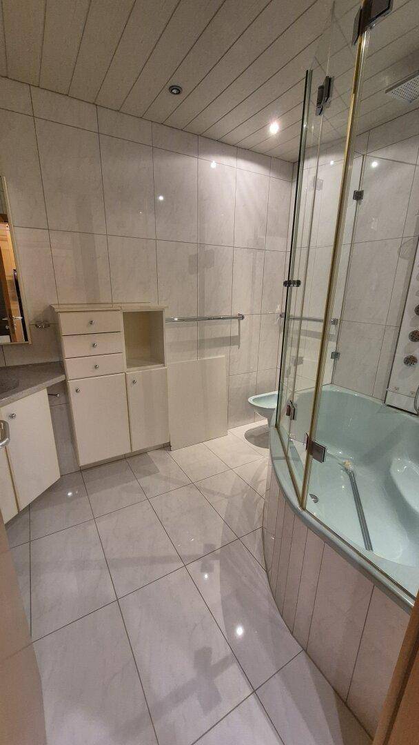 Modern gefliestes Badezimmer mit Eckbadewanne, Glasduschkabine und weißem Waschtischunterschrank.