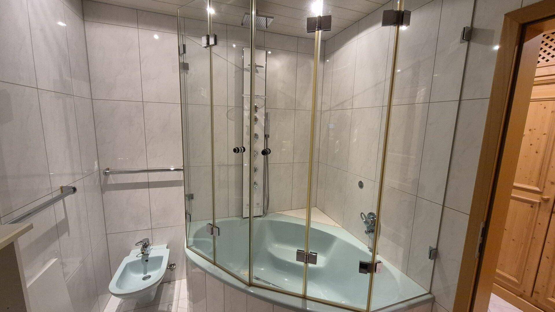 Helles Badezimmer mit Eckbadewanne, Duschkabine, Bidet und modernen Fliesen.