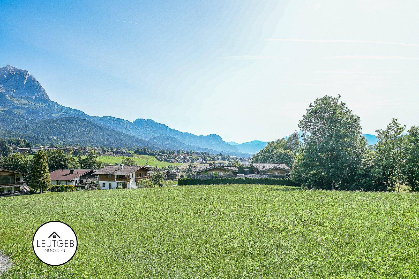 Weitläufige grüne Wiesen mit Blick auf ein charmantes Dorf und die umliegende Berglandschaft.