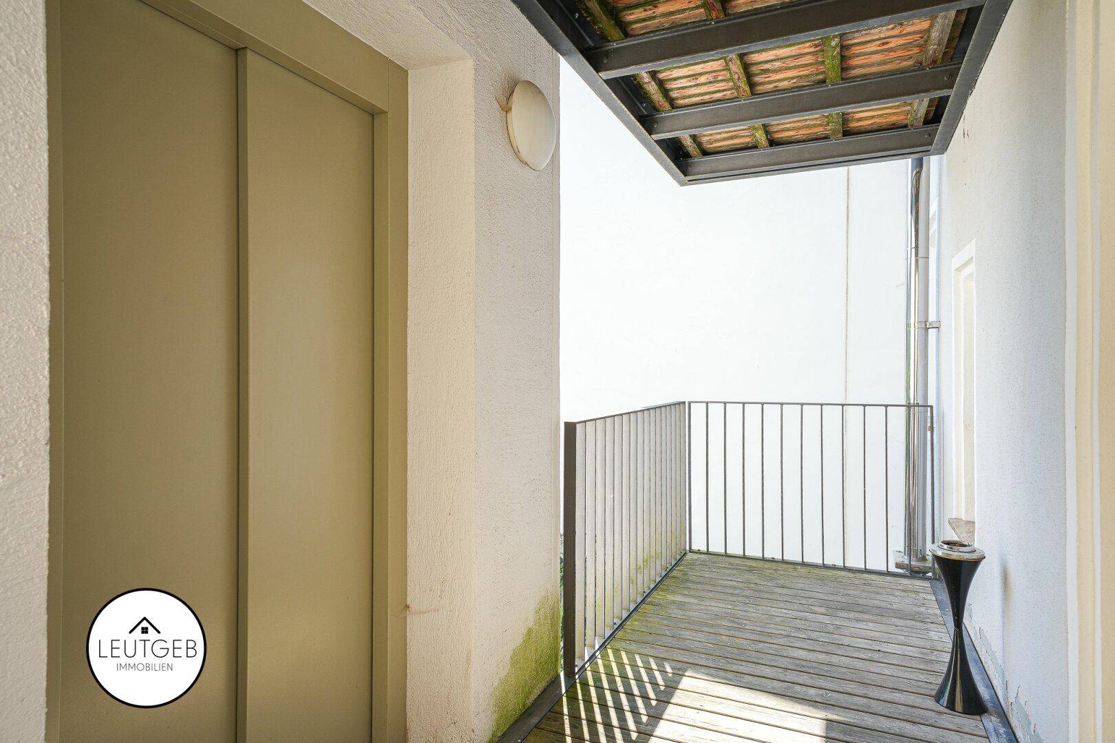 Sonniger Balkon mit Holzboden und Zugang zu einem Aufzug.