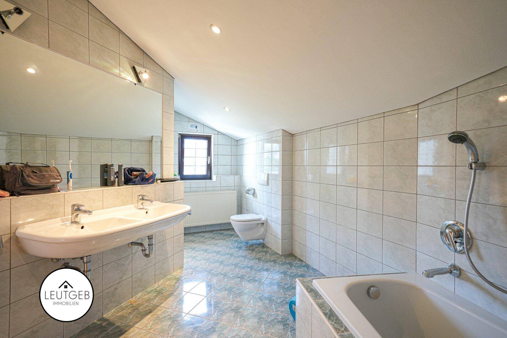 Gefliestes Badezimmer mit Doppelwaschbecken, Badewanne und Fenster.