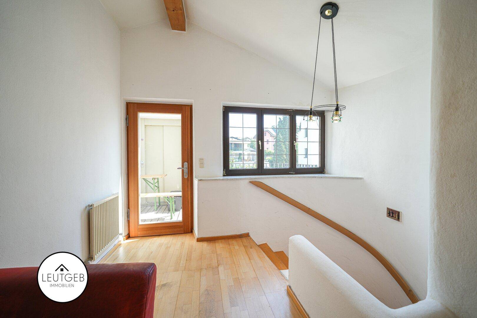 Heller Flur mit Holztreppe, Holzboden und Fenster mit Blick ins Grüne.