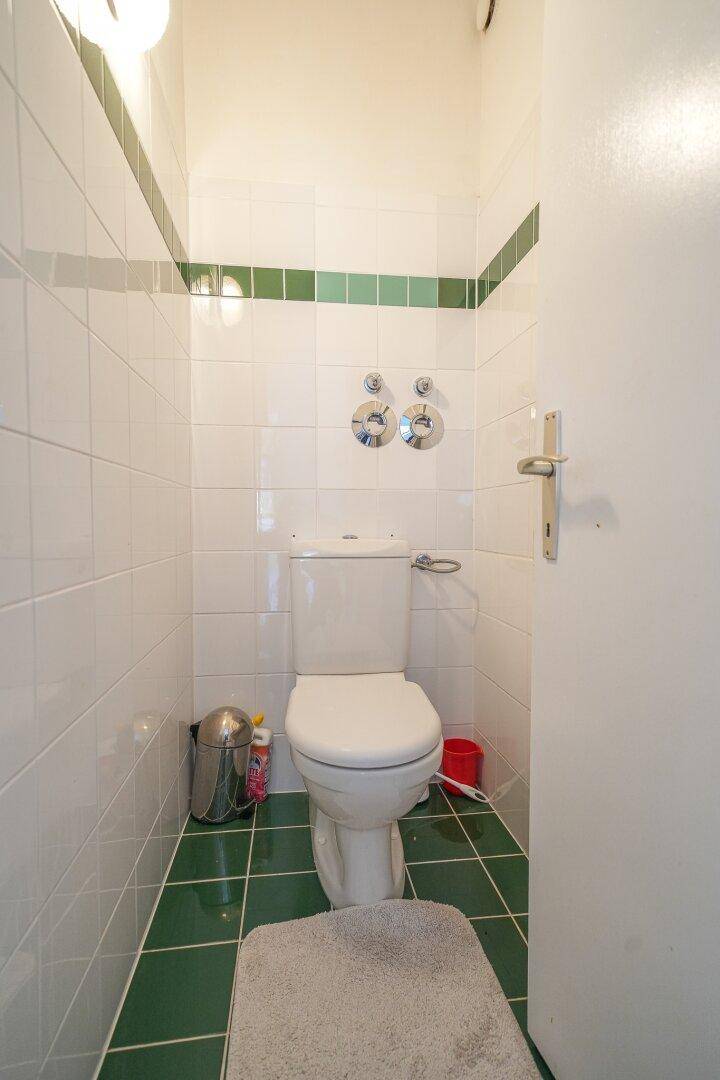 Separate Toilette mit weißen und grünen Fliesen an Wänden und Boden.