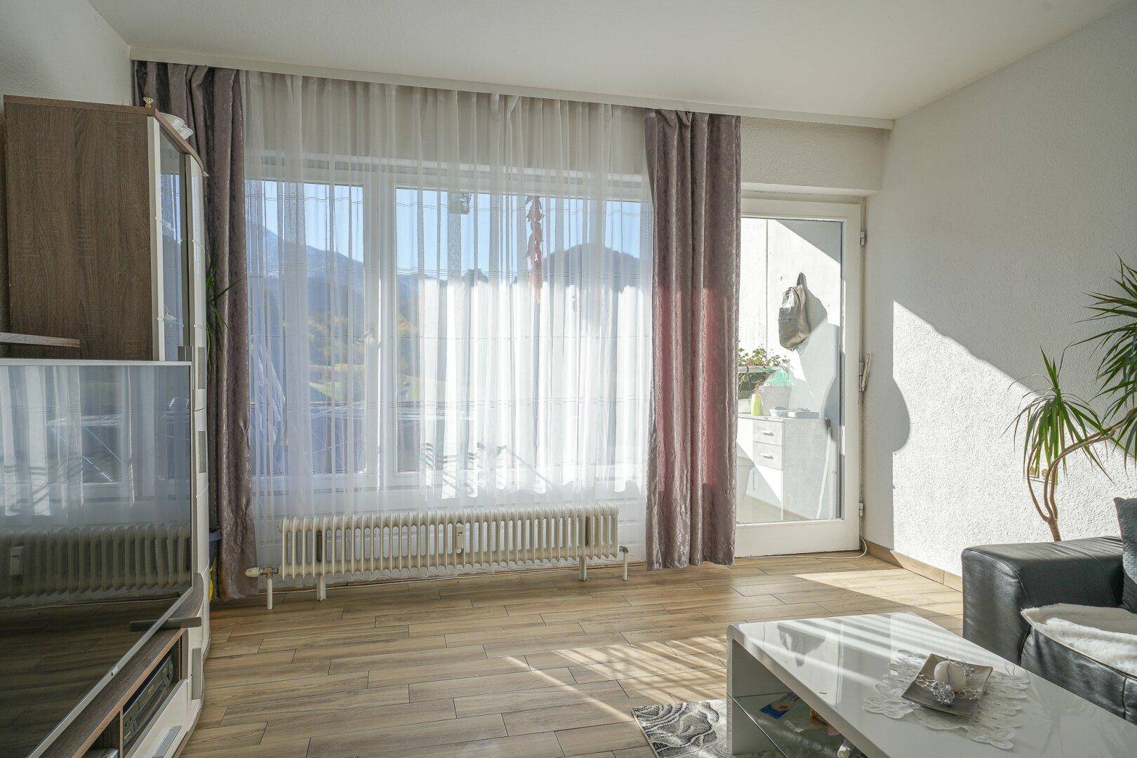 Lichtdurchflutetes Wohnzimmer mit großen Fenstern, Vorhängen und Zugang zu einem Außenbereich.