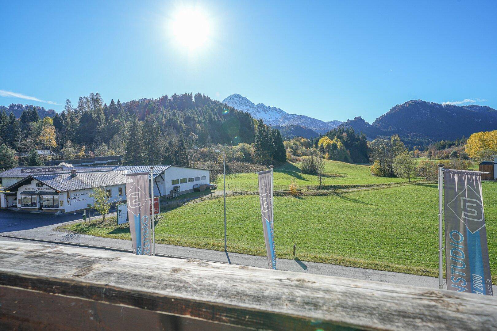Sonniger Ausblick vom Balkon auf grüne Wiesen, Wälder und majestätische Berge.