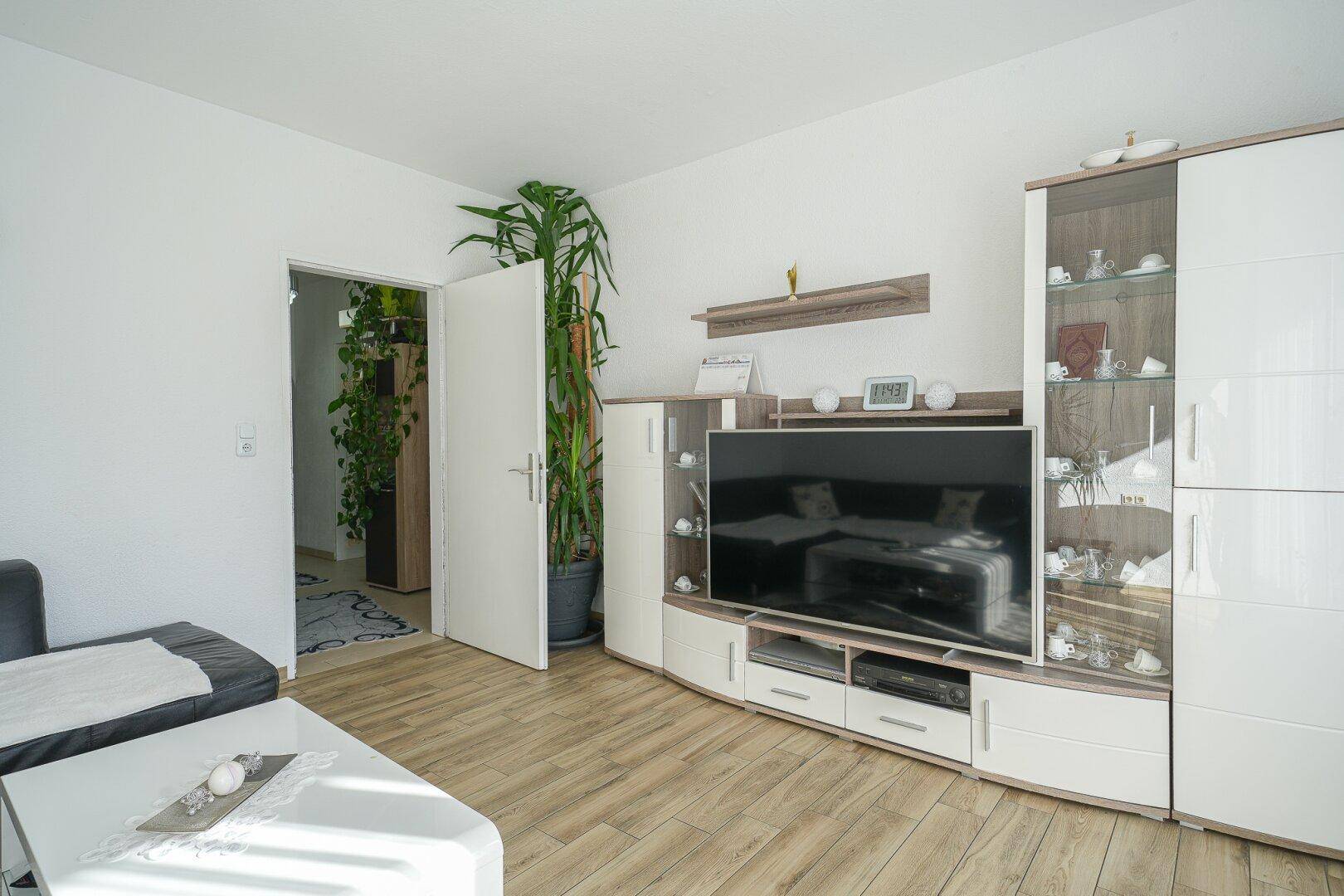 Wohnzimmer mit modernem TV-Möbel, großem Fernseher und hellem Laminatboden, der den Raum aufhellt.