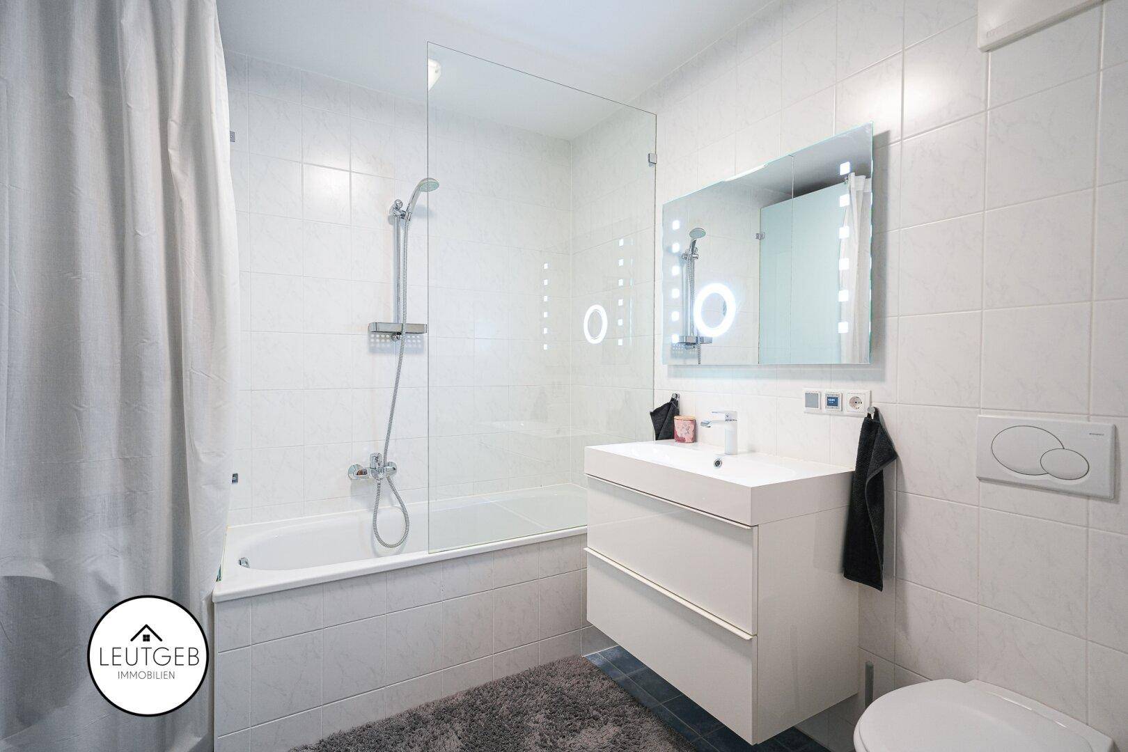 Modernes Badezimmer mit Badewanne, Glasduschwand, schwebendem Waschtisch und weißen Fliesen.
