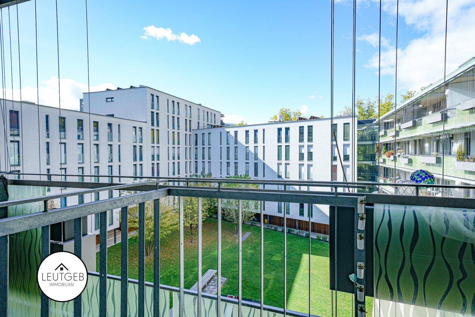 Blick vom Balkon auf einen gepflegten grünen Innenhof, umgeben von modernen Gebäuden.